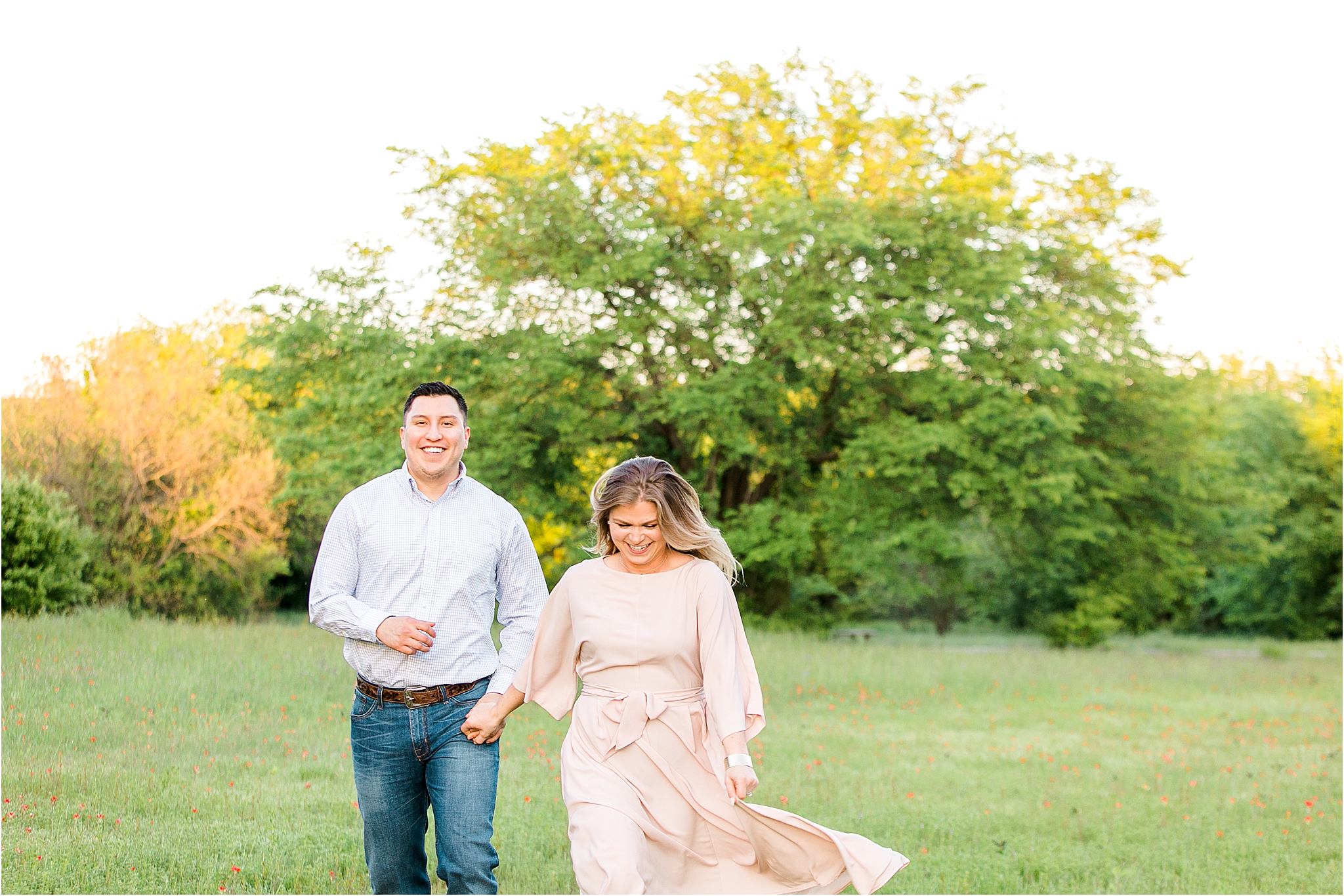 An engaged couple Running through a lush field with trees while laughing during an engagement session in Fort Worth, Texas 