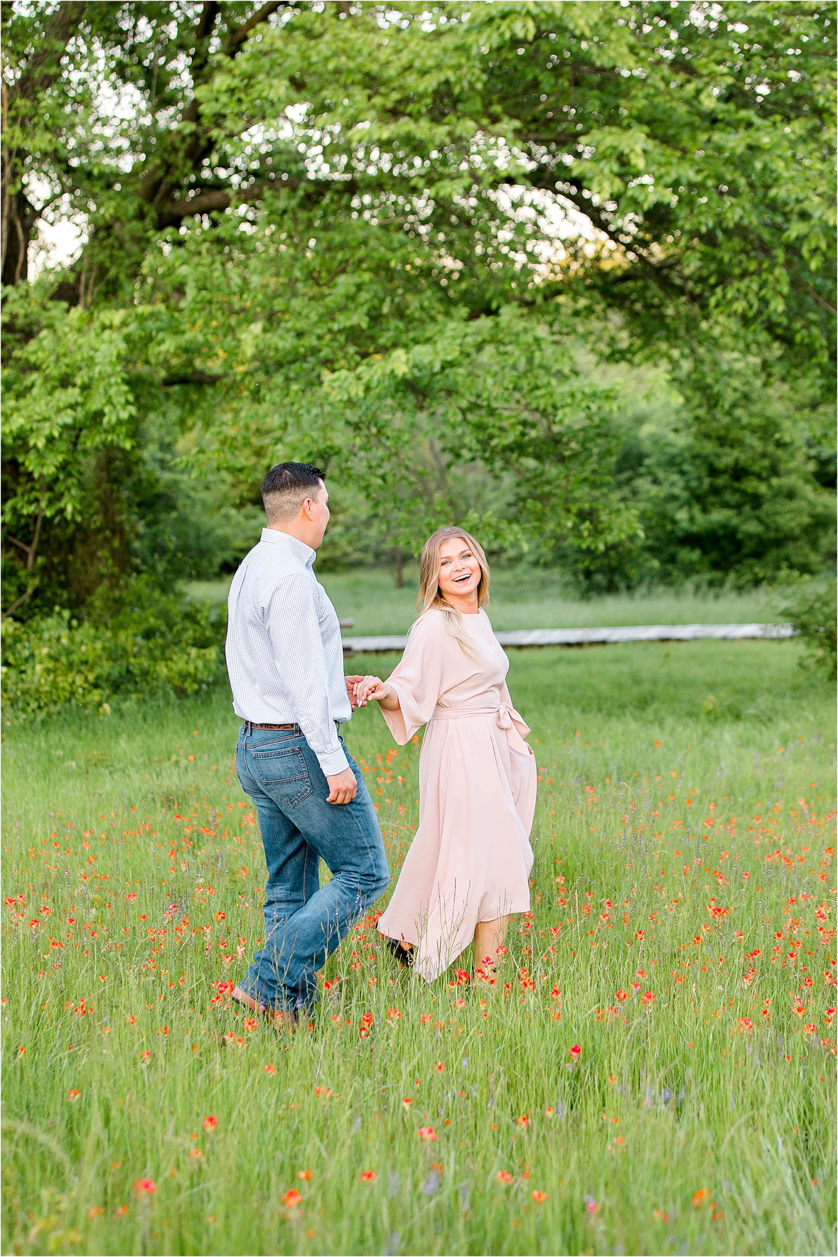 A happy, smiling bride to be pulling her fiance along in a lush field with flowers for their engagement session near Fort Worth, Texas 