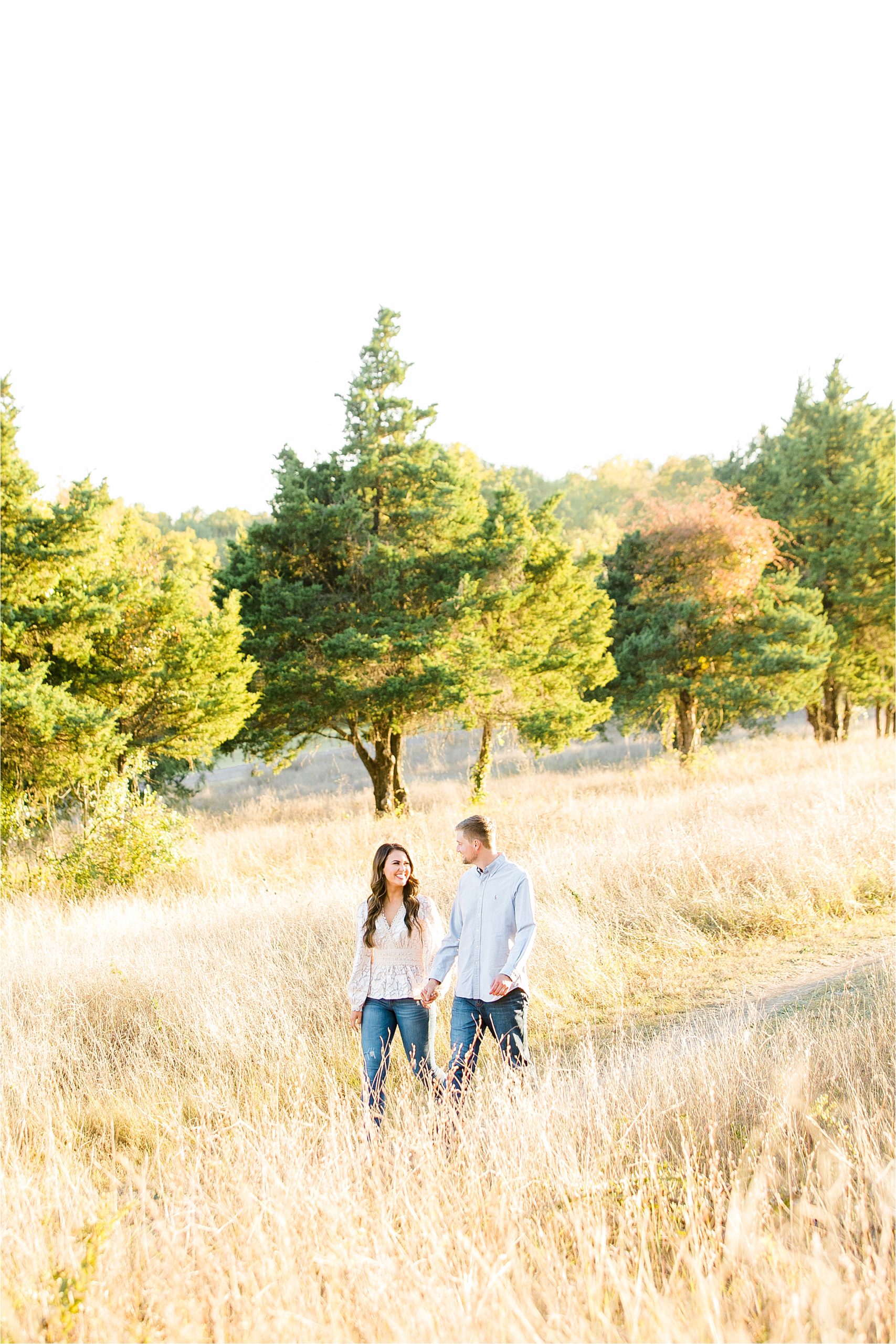 A couple laughing and holding hand in a field with trees behind them just outside McKinney, Texas by Dallas Engagement Photographer Jillian Hogan 