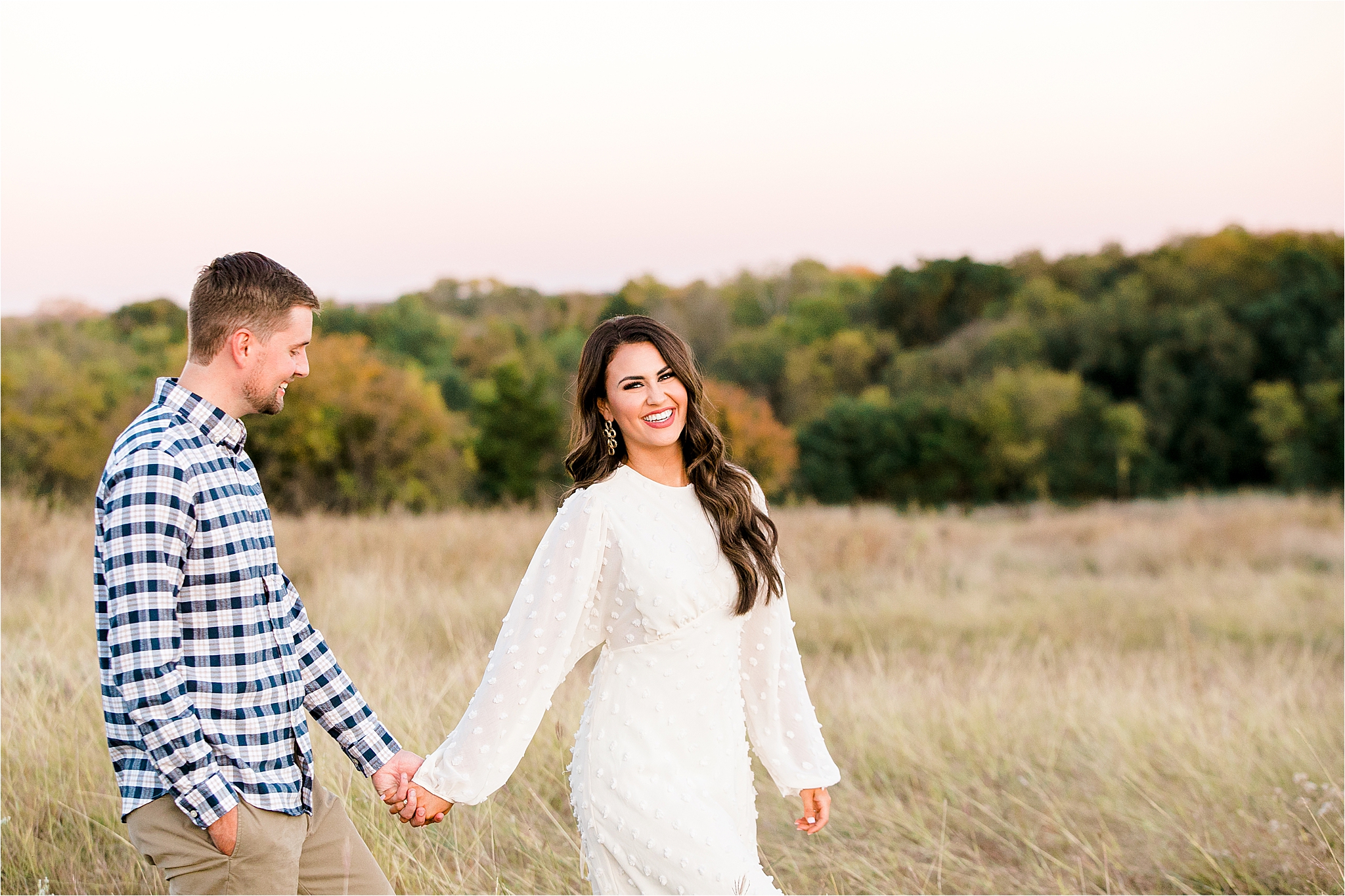 A smiling dallas bride to be pulls her fiance along in a field at sunset during their Fall engagement session 