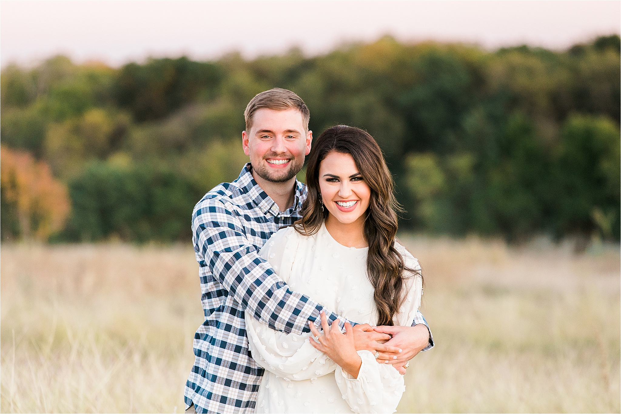 A groom to be hugs his future bride from behind in a field at sunset in McKinney, Teas during their fall engagement session with Dallas Wedding Photographer Jillian Hogan 