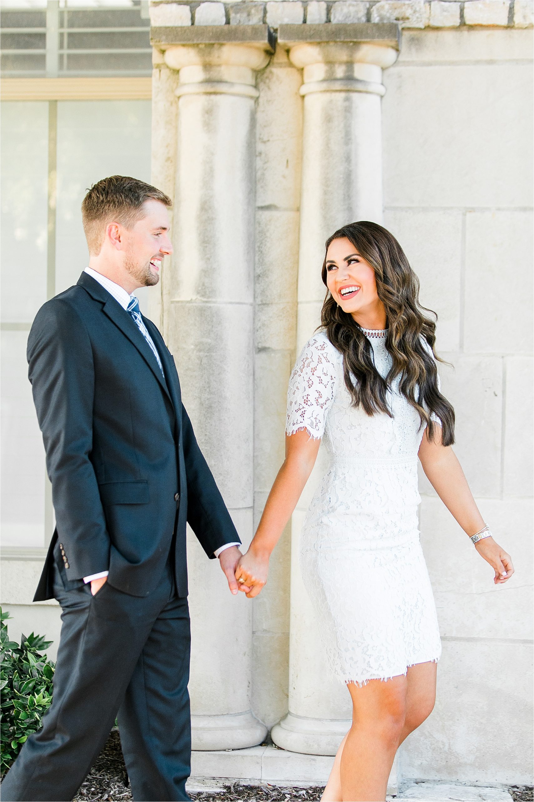 A smiling bride to be with long wavy brown hair holds her fiances hand and looks back at him happily in McKinney, Texas by Dallas Engagement Photographer Jillian Hogan 