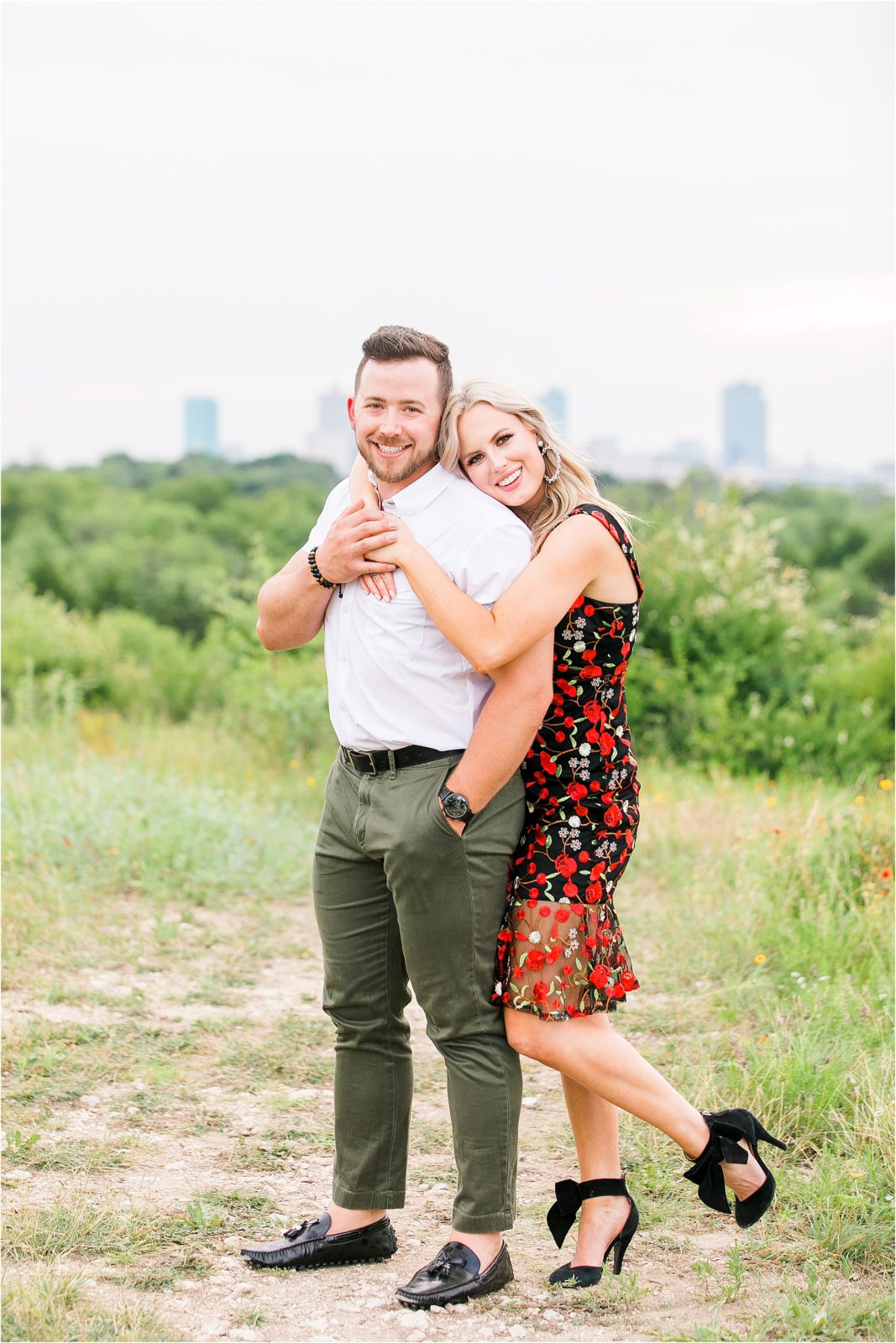 A blond woman hugs her fiance from behind leaning her head on his should at a nature preserve overlooking Fort Worth, Texas during their engagement session 