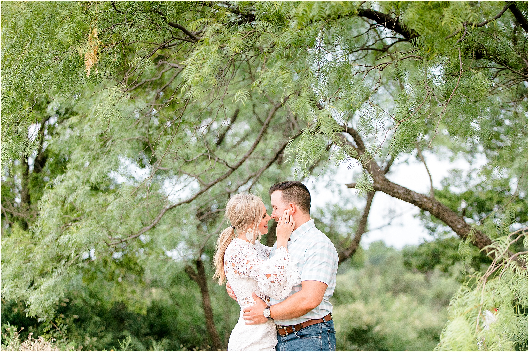 A blond woman in a lace dress puts her hand on her fiance's cheek under a tree during their Tandy Hills Engagement Session 