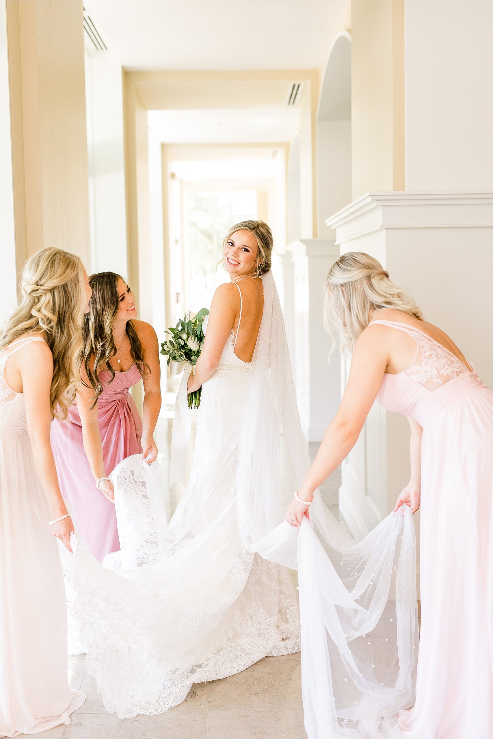 Bridesmaids fix a bride's train at she glances back at the camera on her wedding day at Prestonwood Chapel in Plano, Texas. 