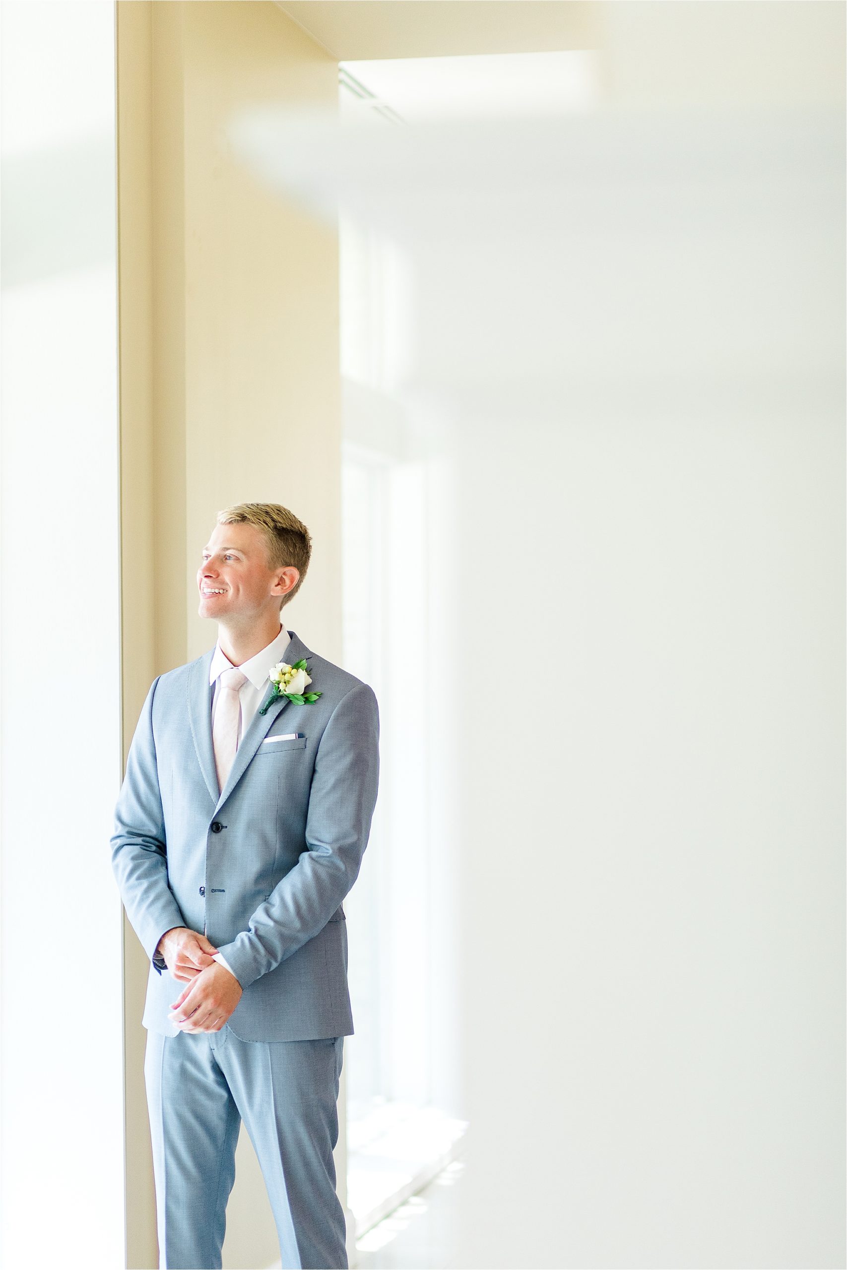 A groom adjusts his cuffs as he stares out the window before his wedding ceremony at prestonwood chapel in Plano, Texas 