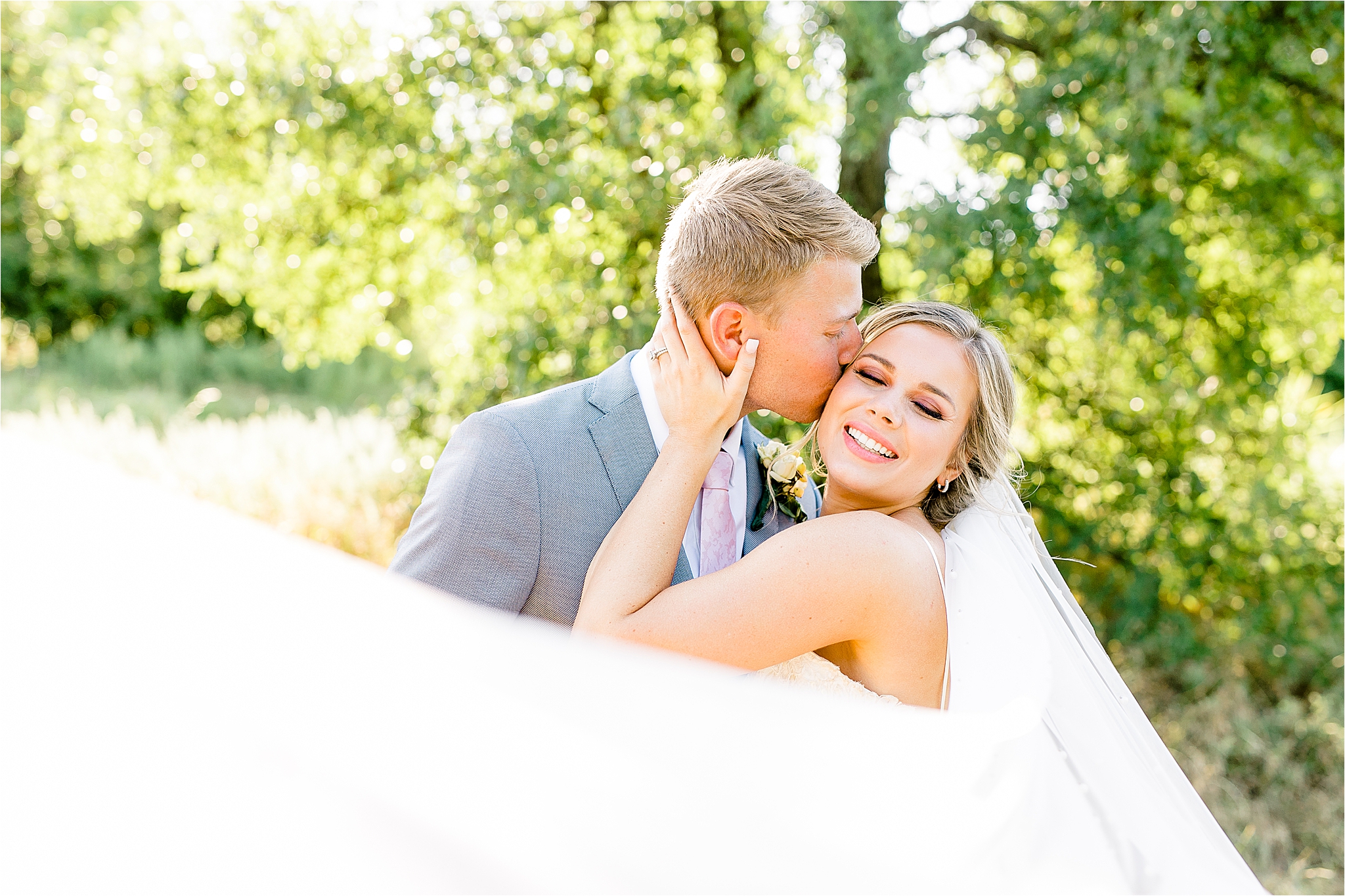 A groom kisses his new bride on the cheek as the veil swoops in front of them during wedding portraits at Arbor Hills Nature Preserve by Dallas Wedding Photographer Jillian Hogan 