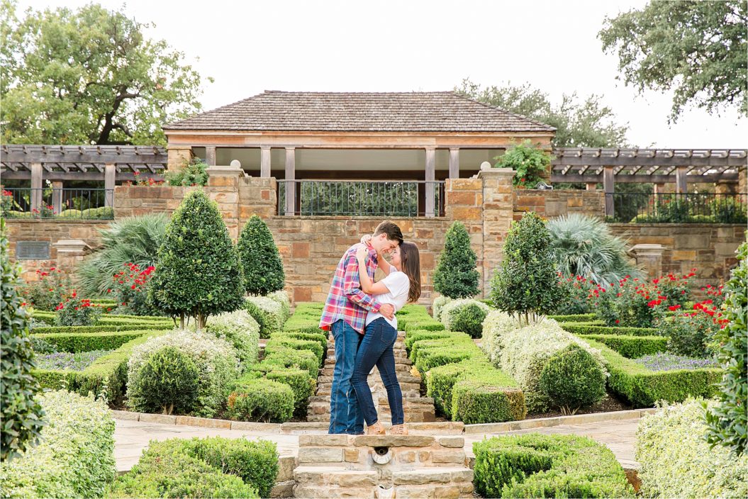 A couple embraces in the main gardens during engagement session at Fort Worth Botanic Gardens