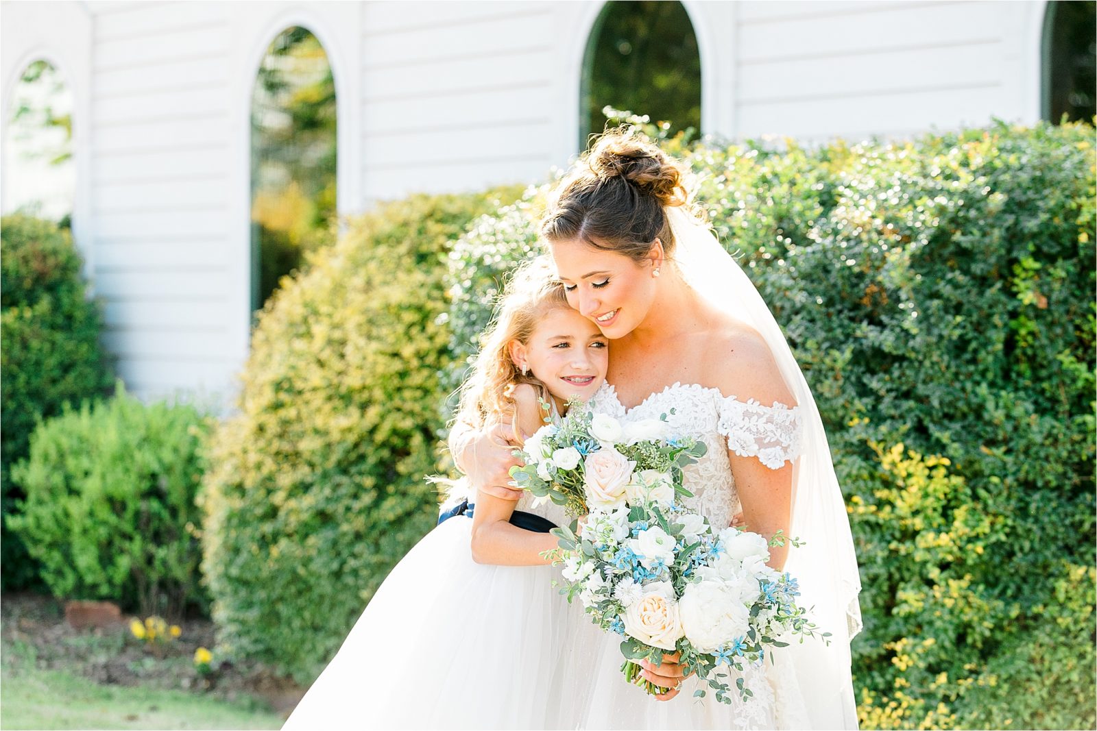 A bride and her little sister share a wedding day hug holding beautiful bouquets right before she says, " I Do."