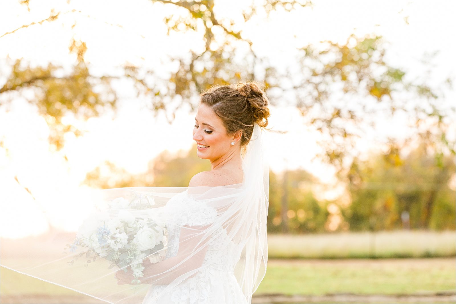 A bride looks back over her shoulder as her wind blows in front of her during sunset bridal portraits with Jillian Hogan Photography 