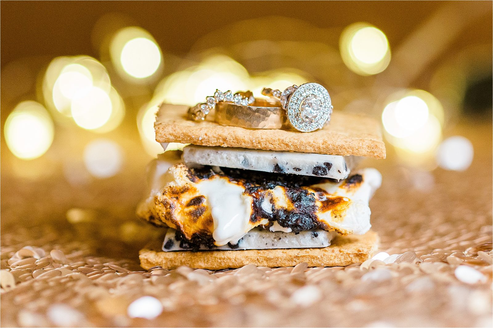 An engagement ring and wedding bands on top of the graham cracker of a smore at a DFW Wedding reception 