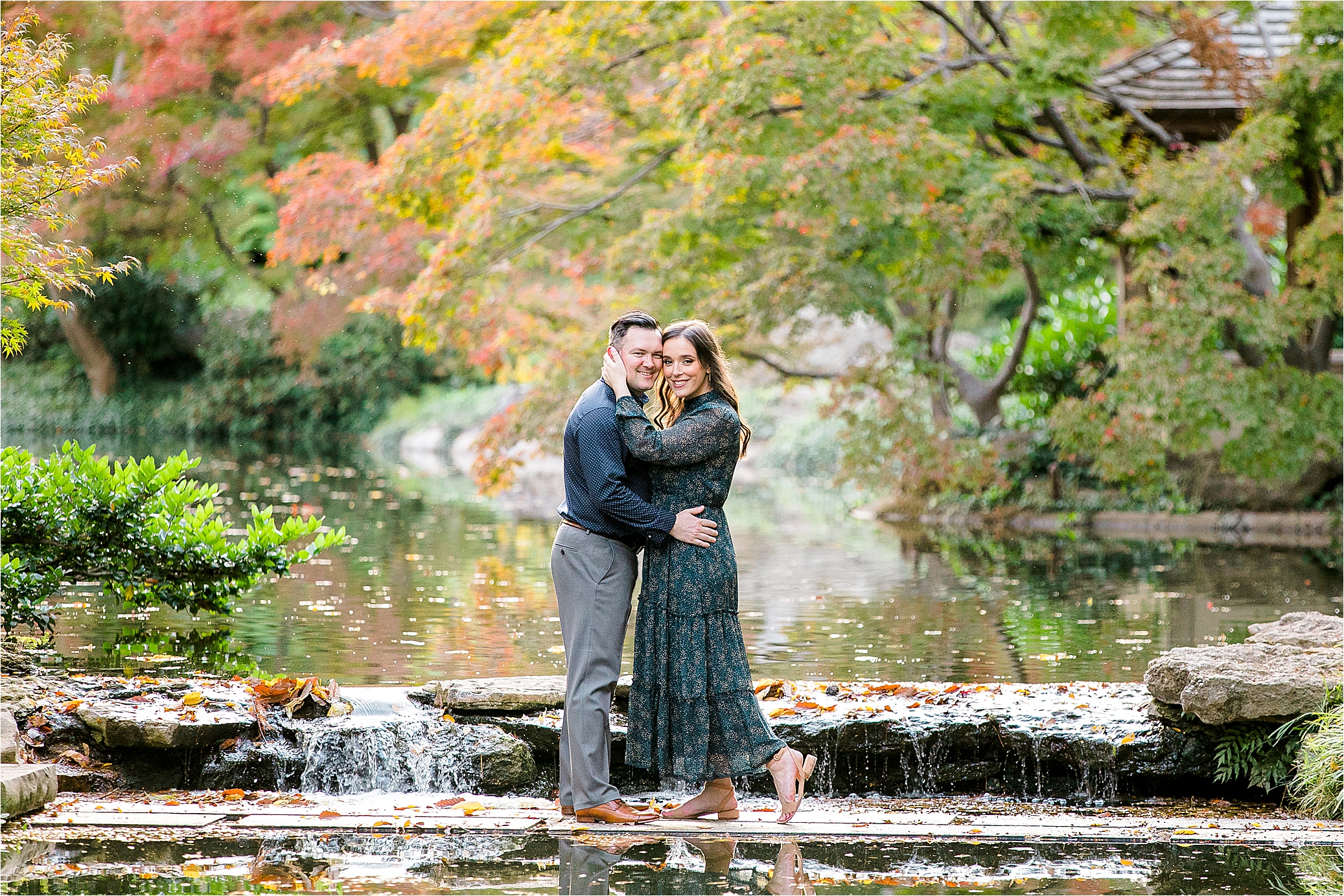 A couple hugs in front of a small waterfall during their engagement session at The Japanese Gardens with DFW Wedding Photographer Jillian Hogan 