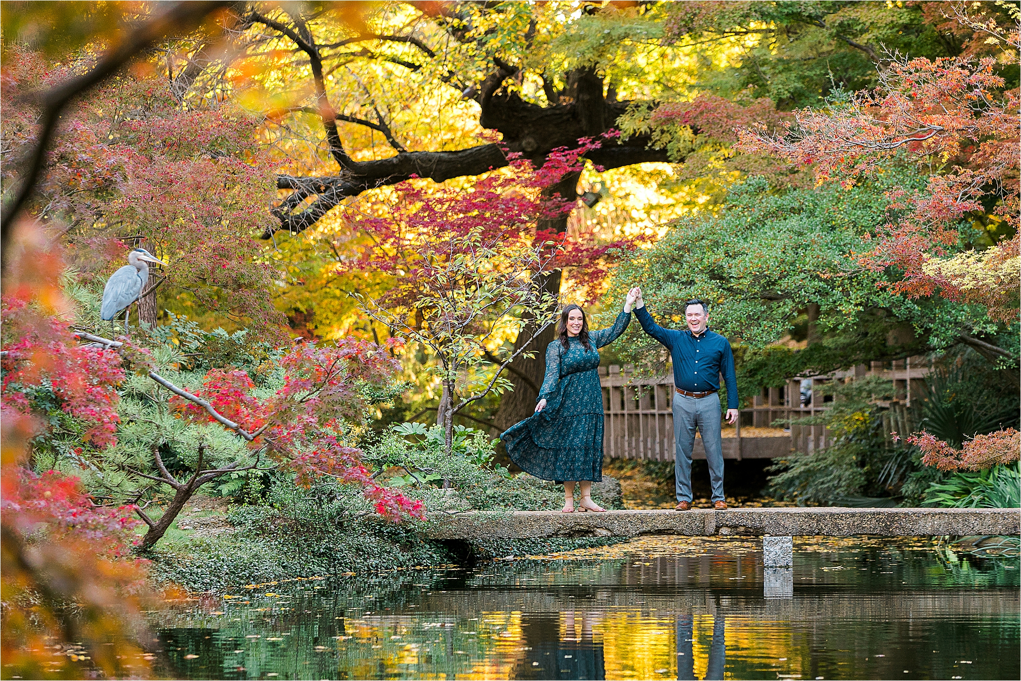 A couple dances on a bridge with a bird in the corner or the photo during their Japanese Garden Engagement Session in Fort Worth, Texas 