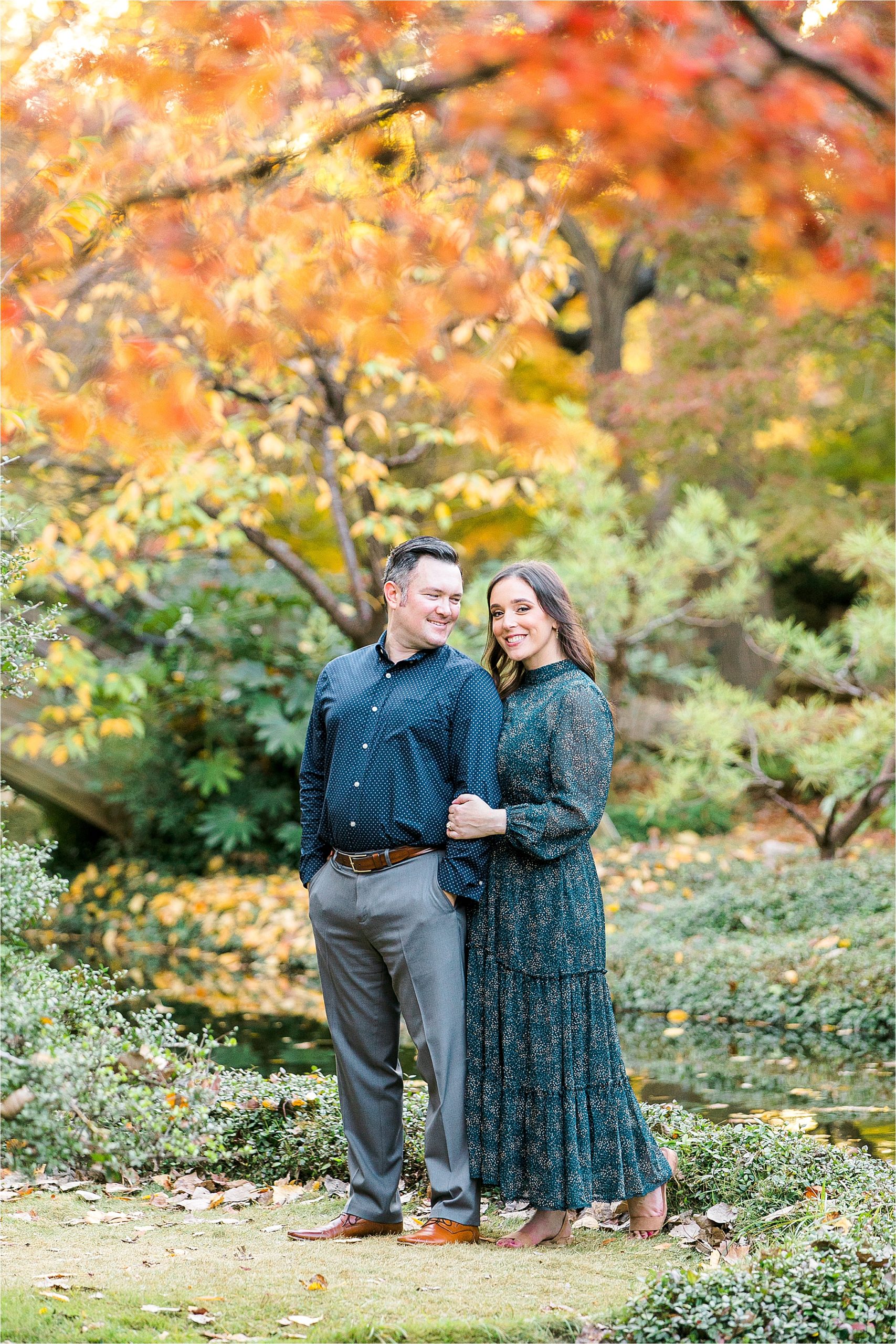 A couple embraces under red and orange leaves in The Japanese Garden during their Fort Worth Engagement session with DFW Wedding Photographer Jillian Hogan 