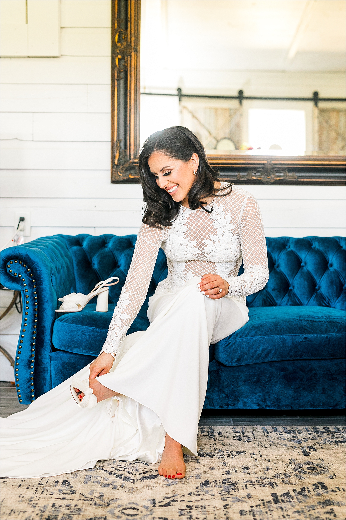 A bride wearing a Justin Alexander wedding dress puts on her wedding shoes on a blue couch at Pineway Farms with San Antonio Wedding Photographer JIllian Hogan 