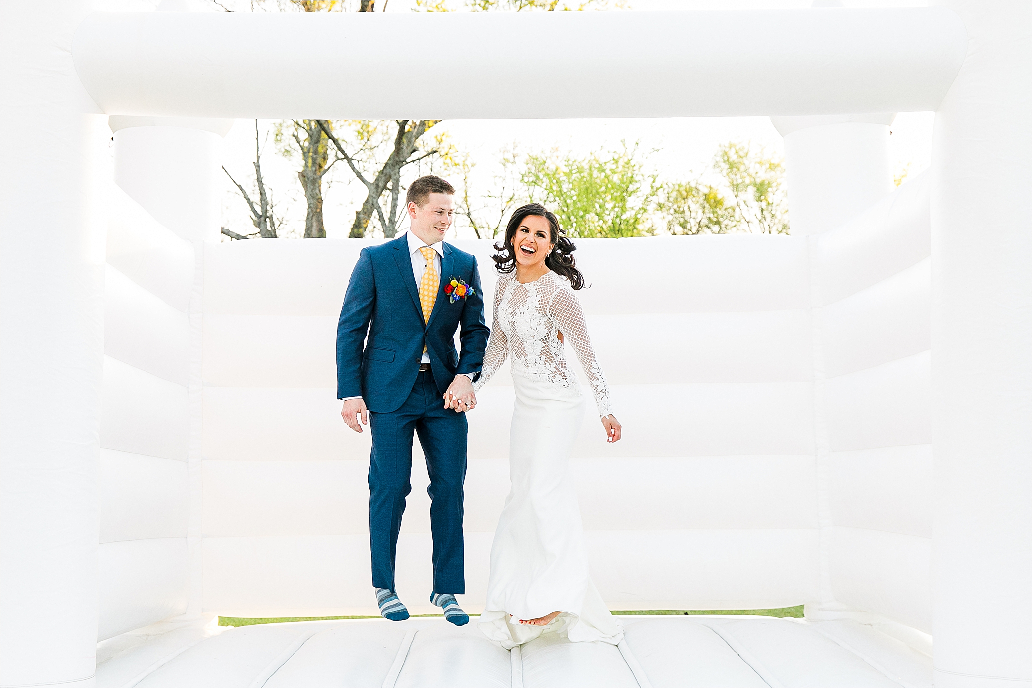 A bride laughs as she jumps in a bounce house with her husband on their wedding day at PIneway Farms with Hill Country Wedding Photographer Jillian Hogan 