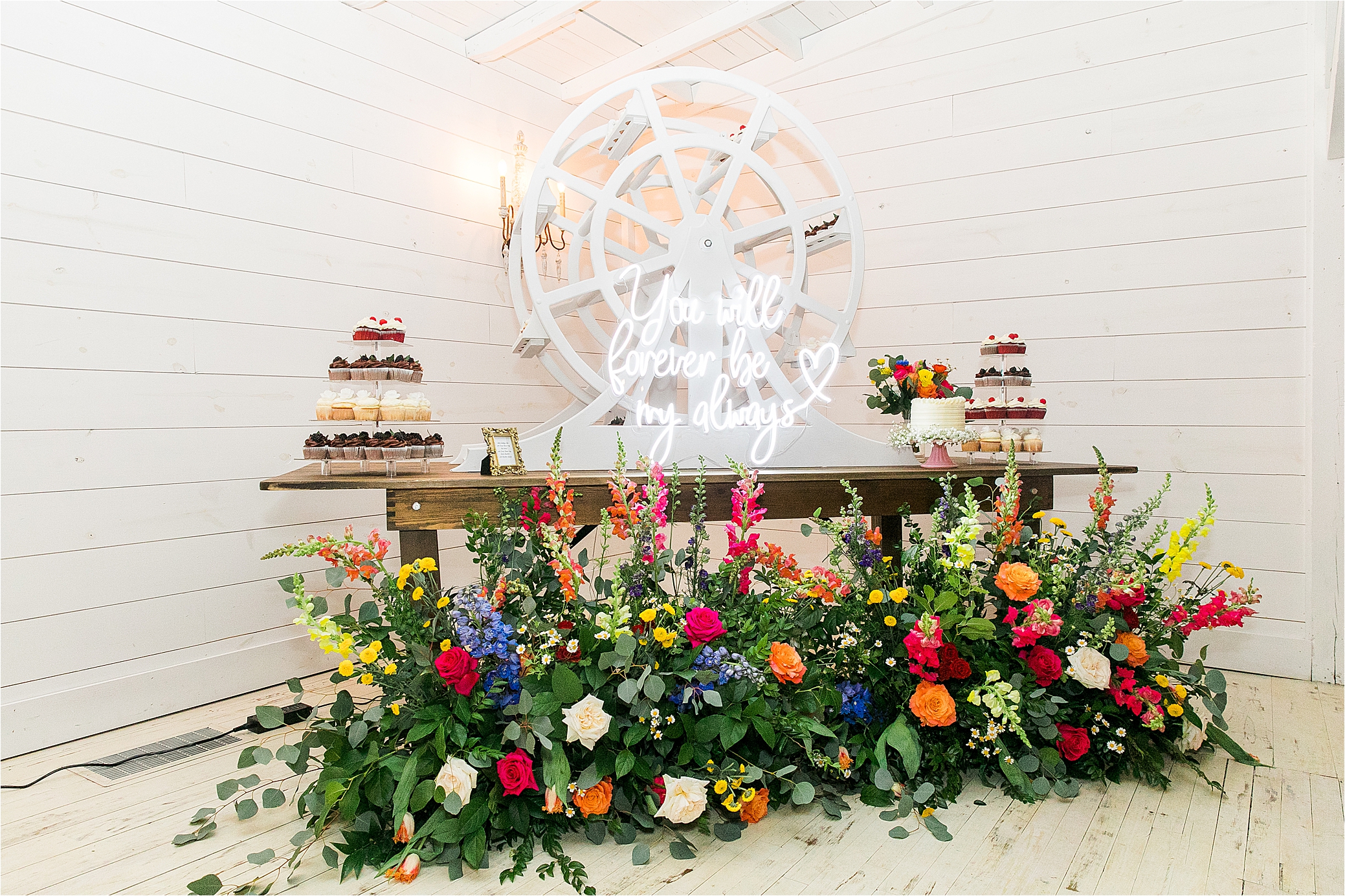 A ferris wheel cake display, a neon sign and colorful flowers around cupcakes and wedding cake 