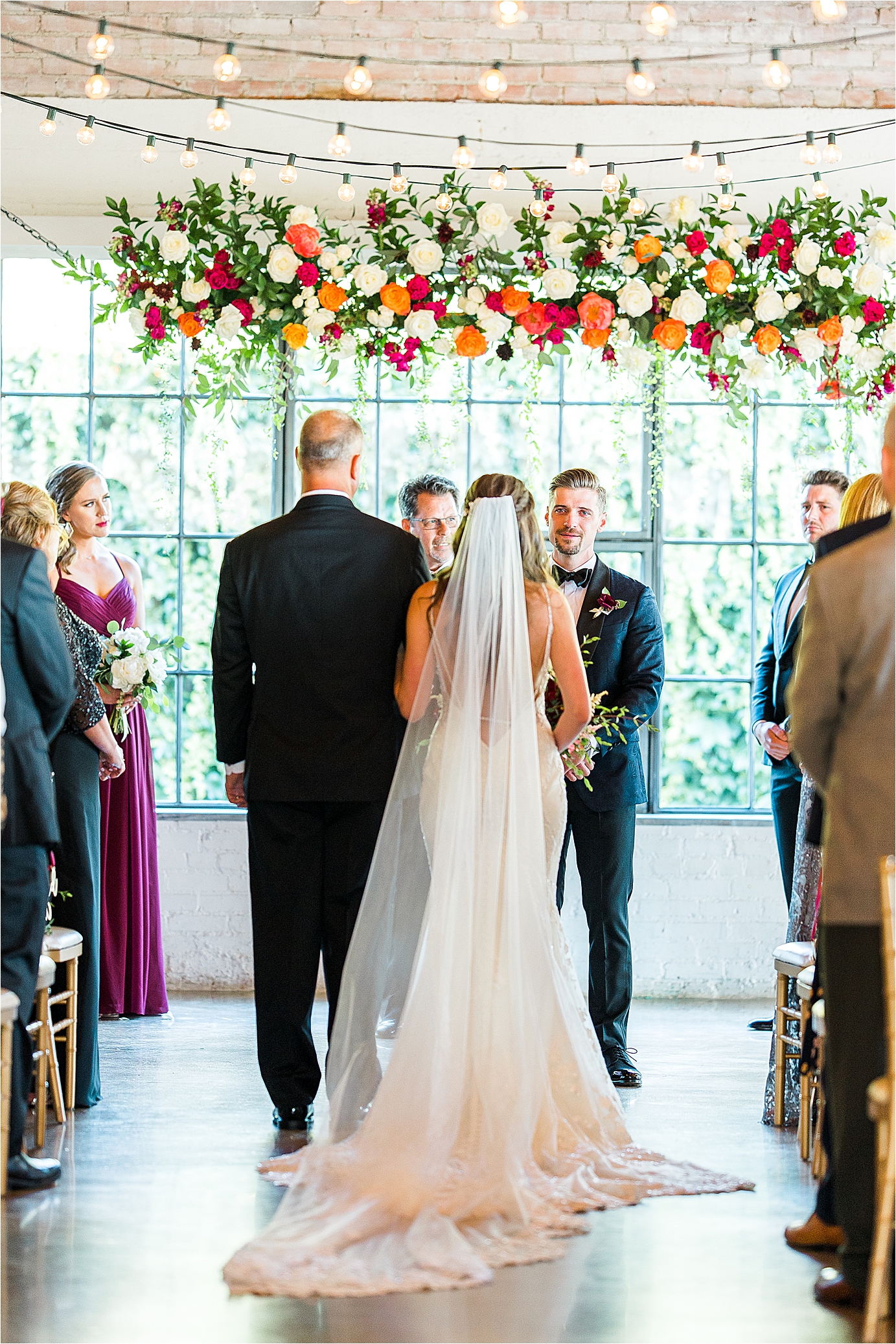 A groom smiles at his bride as her dad walks her down the aisle for their Summer Hickory Street Annex Wedding day