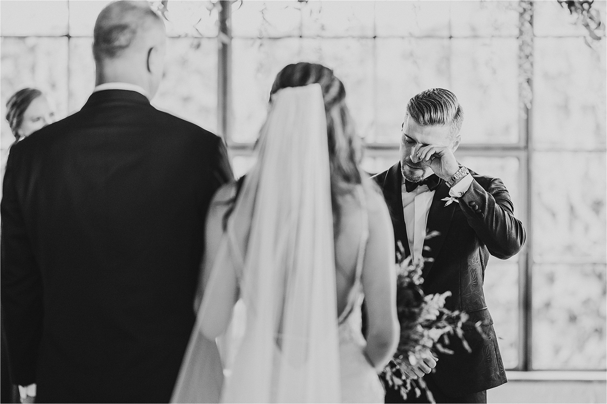 A groom wipes his tears as he sees his bride for the first time down the aisle on their summer wedding day at Hickory Street Annex in Dallas, Texas 
