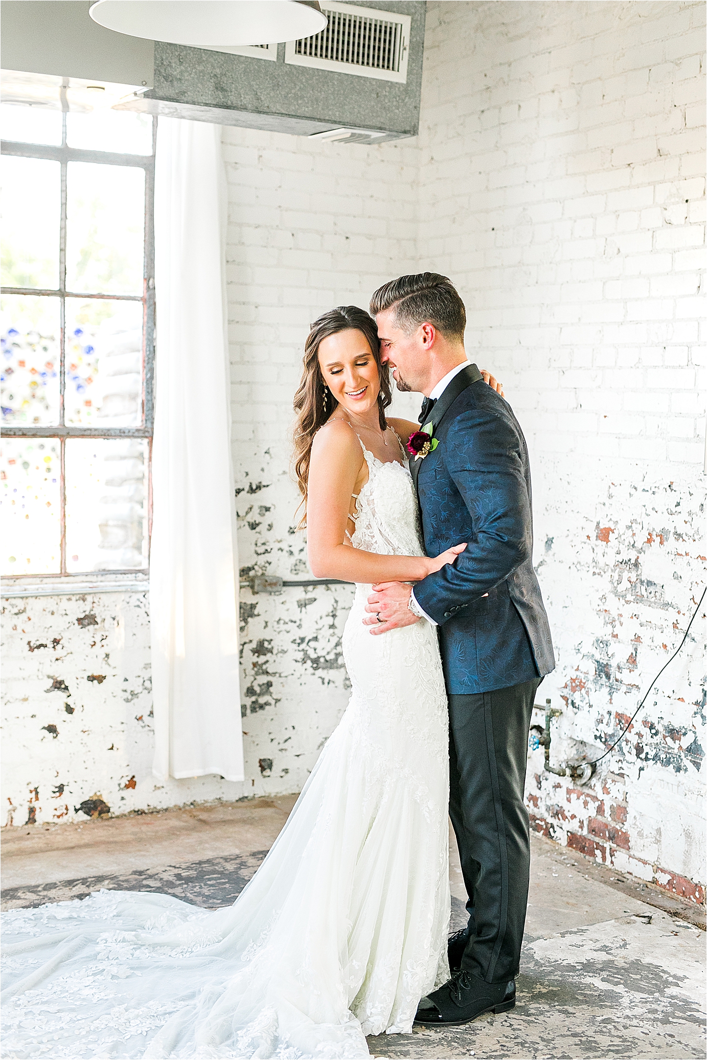 A groom nuzzles and hugs his bride in a bright, white brick room at Hickory Street Annex in Dallas, Texas 