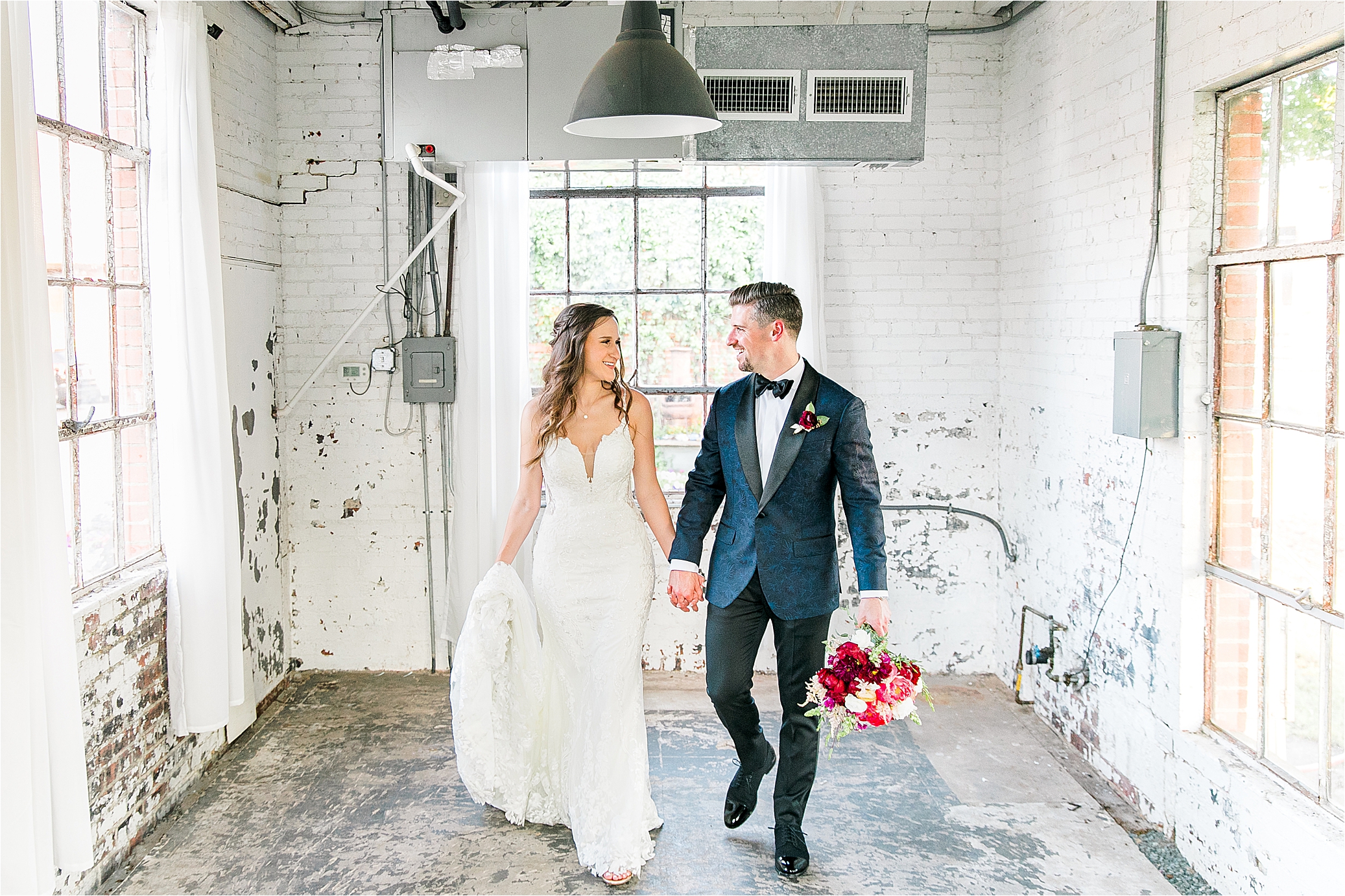 A newlywed couple smiles at each other and holds hands as they walk in a bright, brick building at HIckory Street Annex in Dallas, Texas