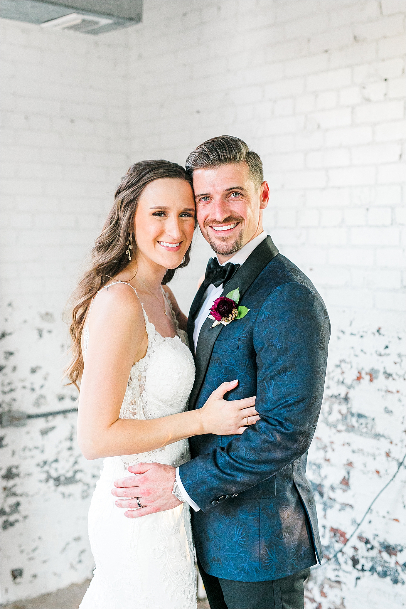 A newlywed couple smiles big at the camera during their wedding day portraits in a white, brick room at Hickory Street Annex in Dallas, Texas 