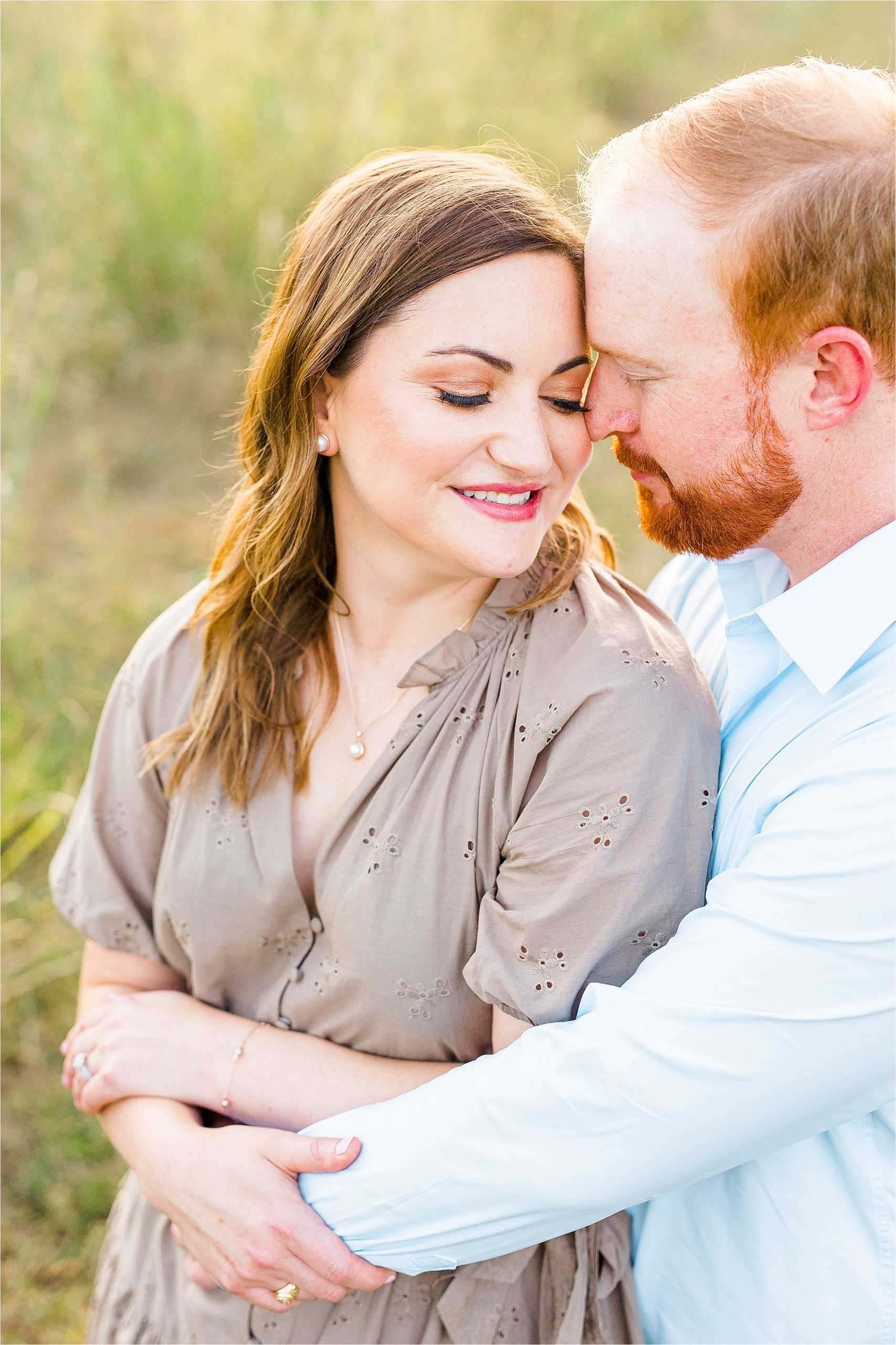 A bride to be snuggles into her fiance as he hugs her during their summer Hill country engagement session at Cibolo Creek Nature Center in Boerne, Texas