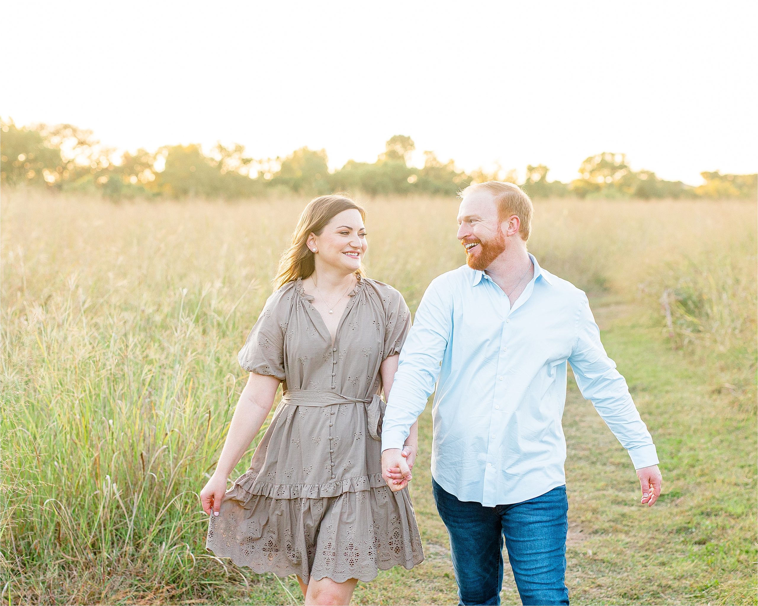 An engaged couple holds hands and laughs in a field at sunset during their portrait session in San Antonio, Texas