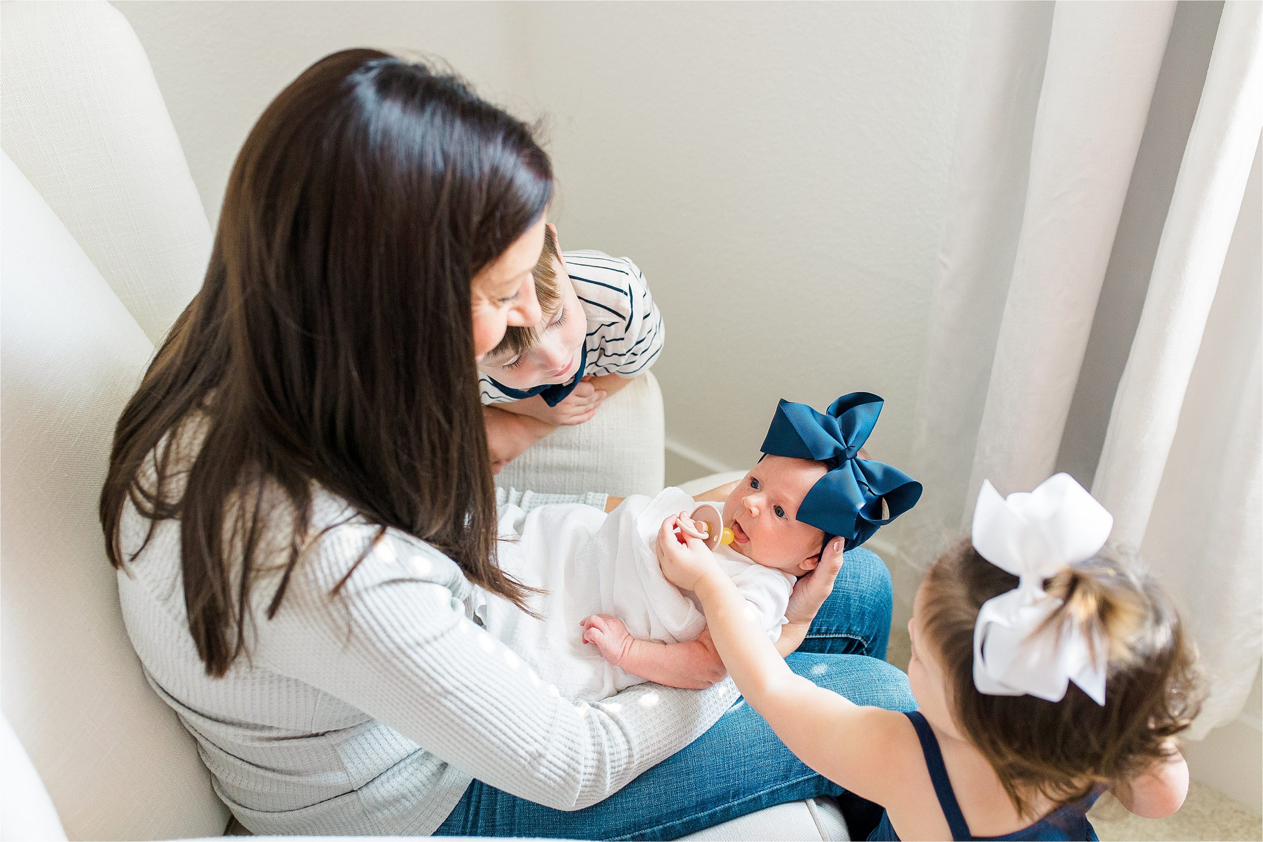 A big sister gives her newborn sister a pacifier while mom and brother look on during their in home lifestyle newborn photos in San Antonio, Texas 