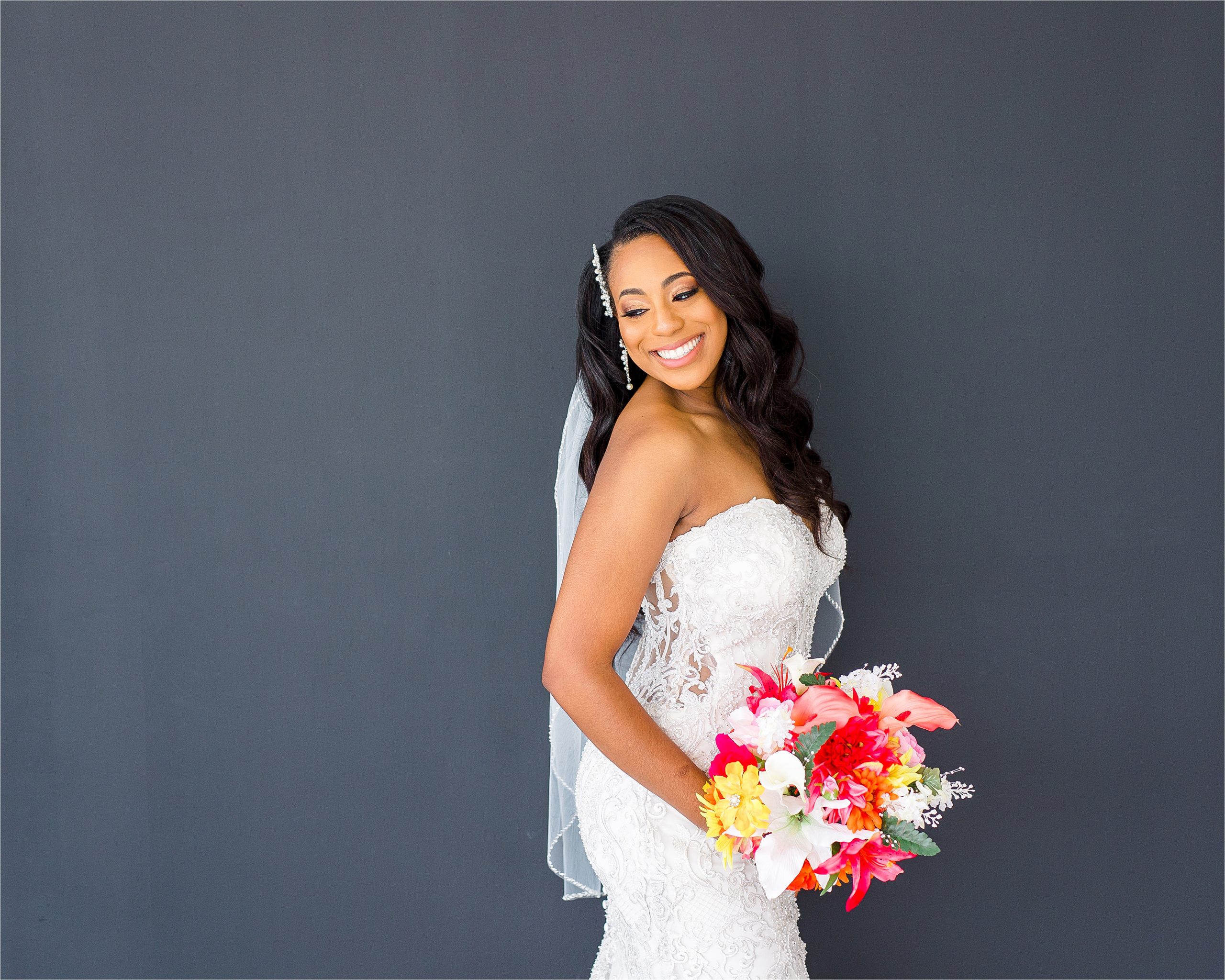 A bride poses looking back over her shoulder in front of a black background with colorful, summer bouquet for her San Antonio Studio Bridal Session with Wedding Photographer Jillian Hogan