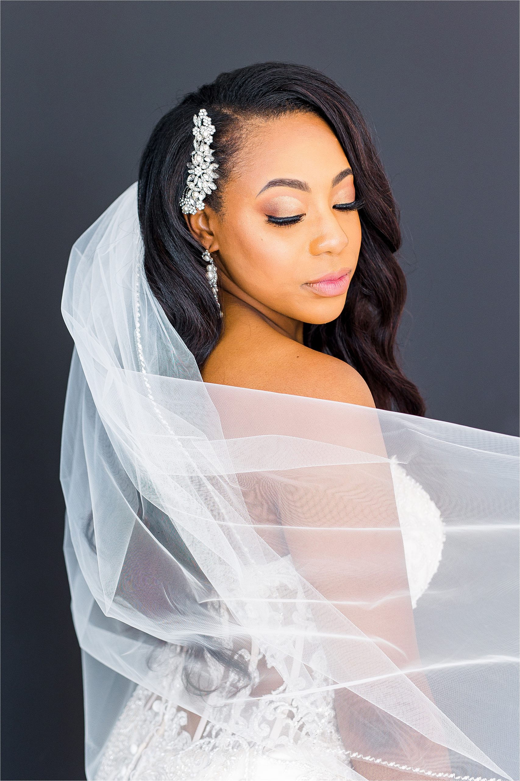 A closeup of a beautiful black bride looking back over her shoulder with her veil covering her arm during her studio bridal portraits in San Antonio, Texas 
