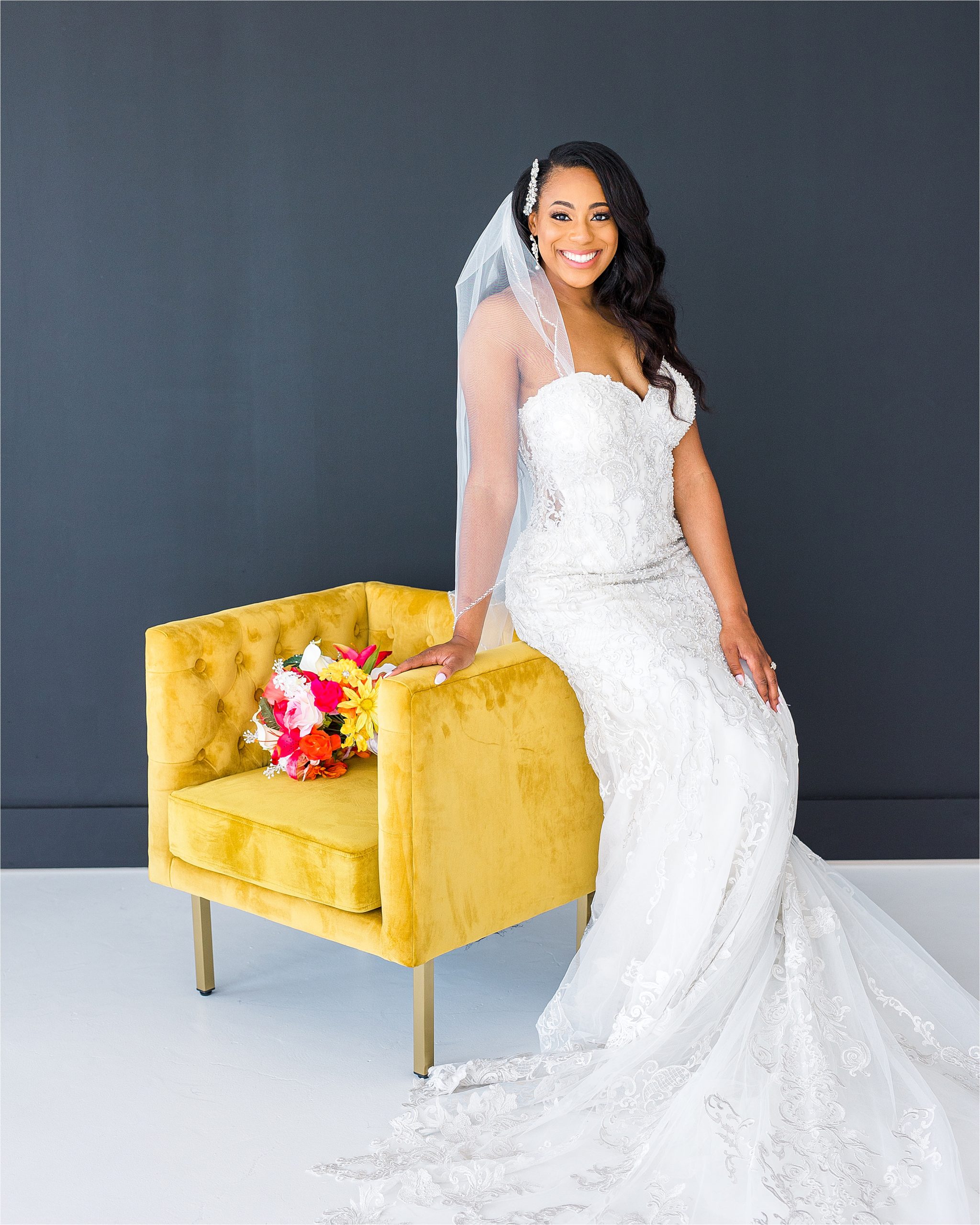 A beautiful black bride leans on a mustard yellow chair in a lace wedding dress, veil and headpiece for her San Antonio Bridal Portraits with Wedding Photographer Jillian Hogan 