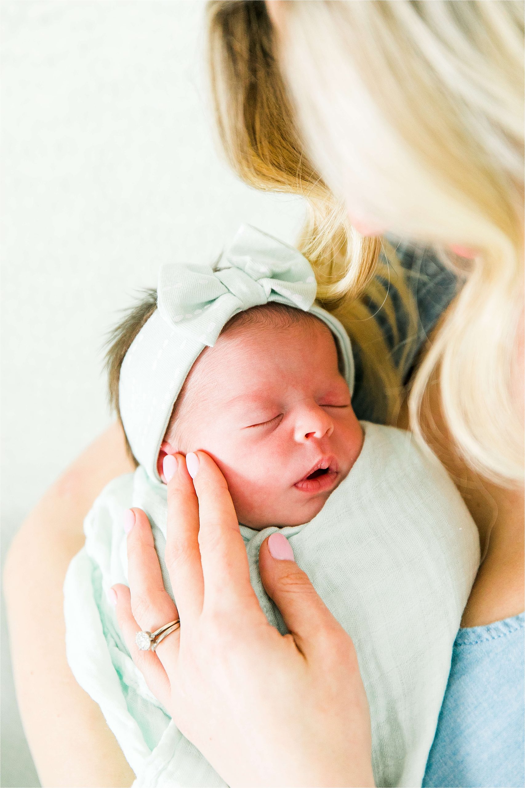 A mom loves on her newborn daughters cheeks as she sleeps in her green swaddle during their lifestyle newborn session with Boerne Photographer Jilian Hogan 