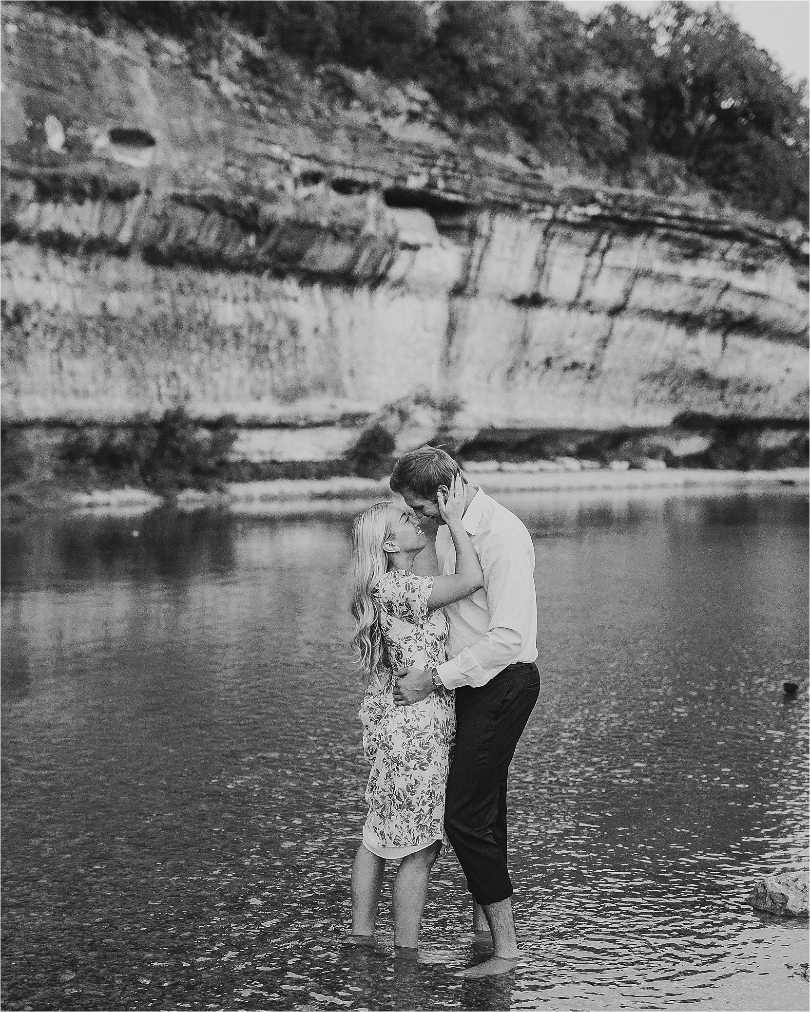An engaged couple embraces in the water during their hill country engagement with a large rock cliff in the background at Guadalupe River State Park with Jillian Hogan Photography 