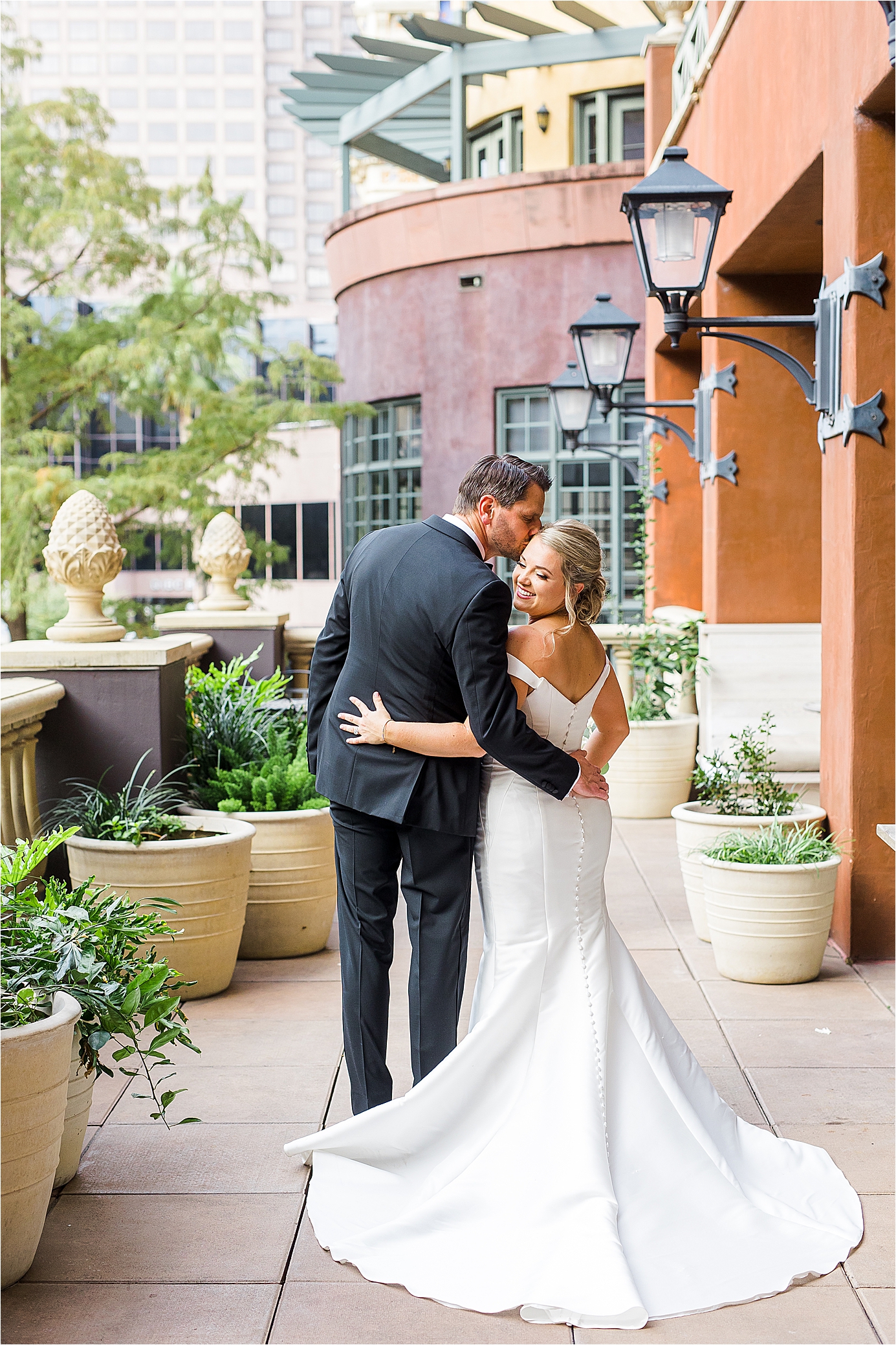 A groom kisses his bride on her forhead as we peek a the back of her dress on the Valencia Hotel Patio in San Antonio, Texas 