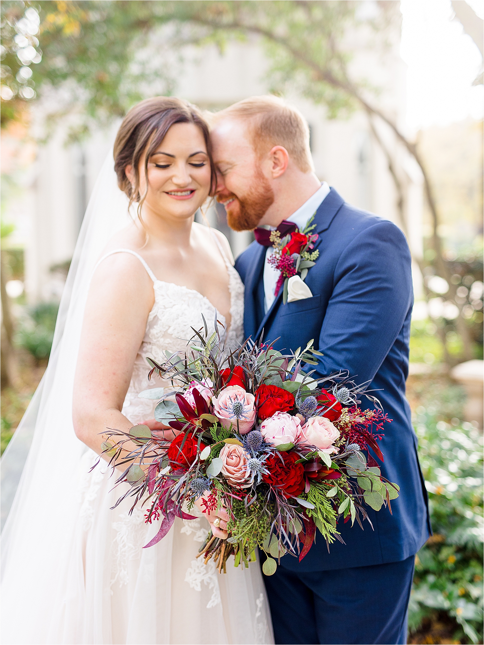 A groom in a navy suite nuzzles into his bride to be as she holds a colorful wedding bouquet and smiles during her San Antonio Wedding 