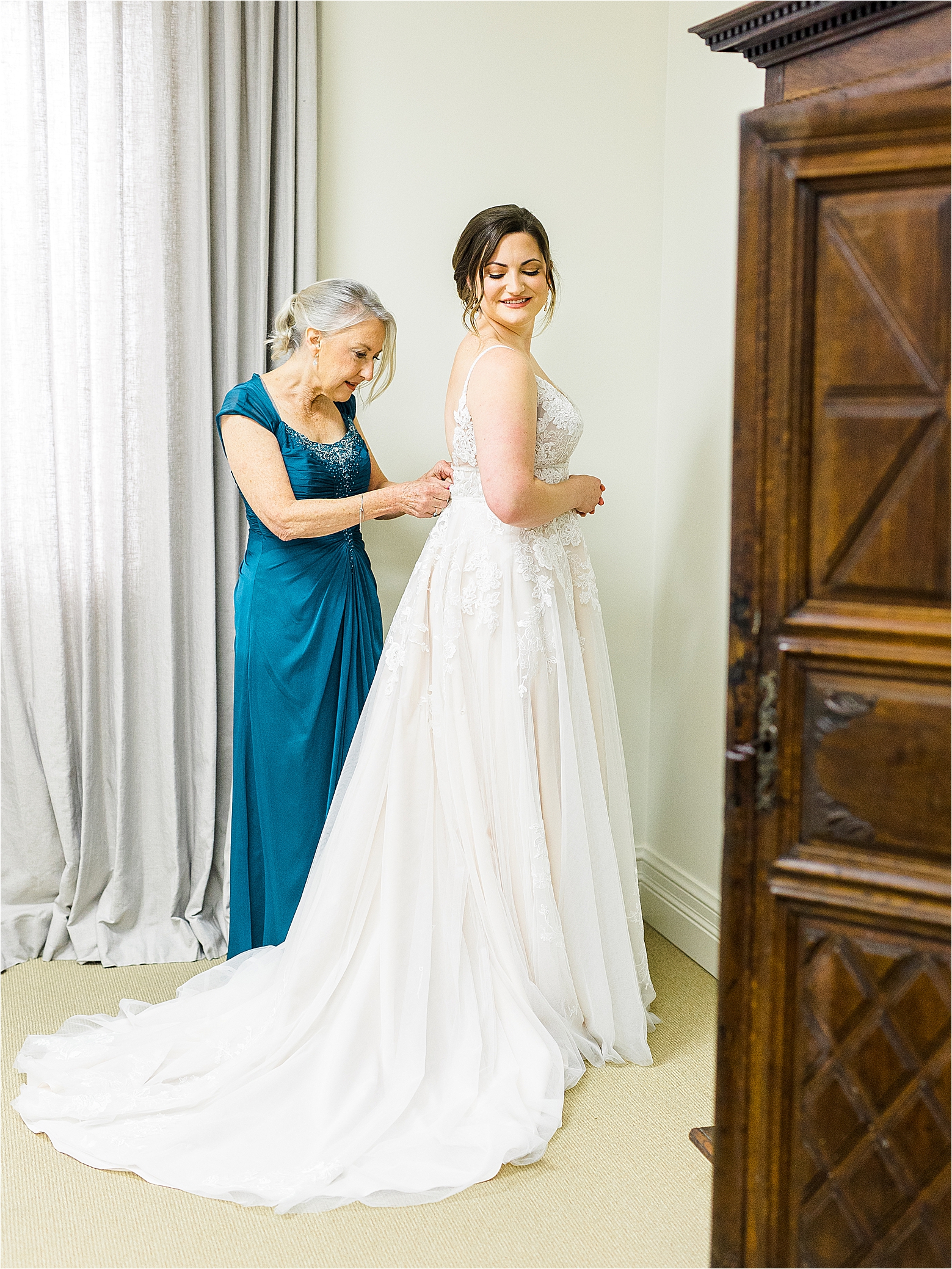A mother of the bride in a blue dress zips up her daughter as she glances over her shoulder in the bridal suite at Alamo Heights United Methodist Church in San Antonio, Texas 