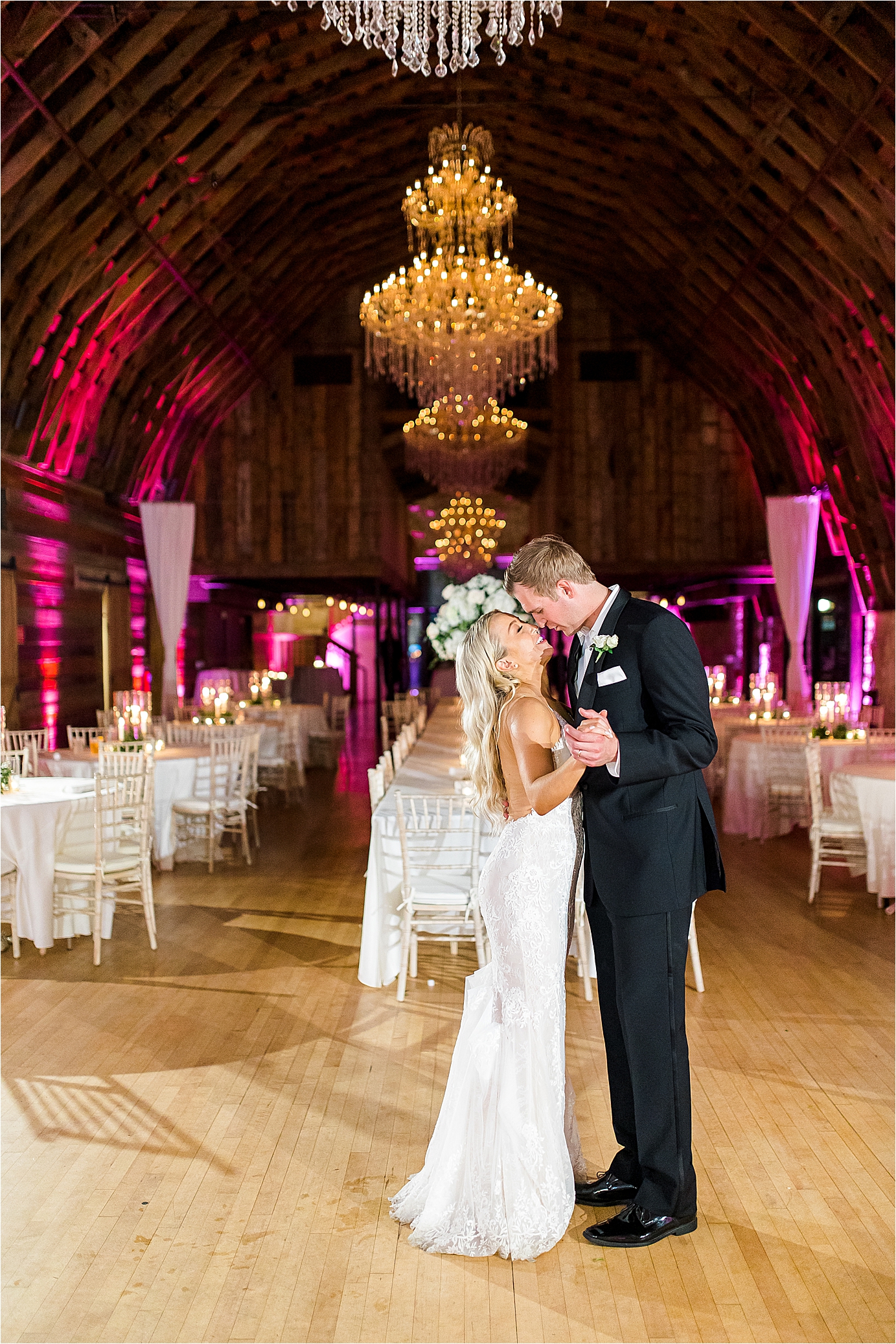 A bride and groom share a private last dance with chandeliers and pink lights surrounding them as they nuzzle close to wrap up their barn style wedding reception at Brodie Homestead in Austin, Texas