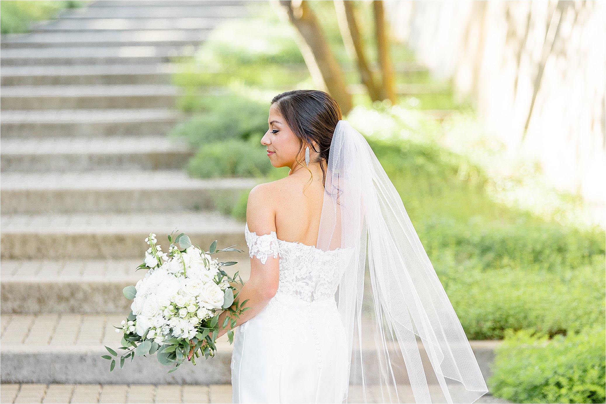A bride looks over he shoulder holding a white bouquet at San Antonio Botanical Garden