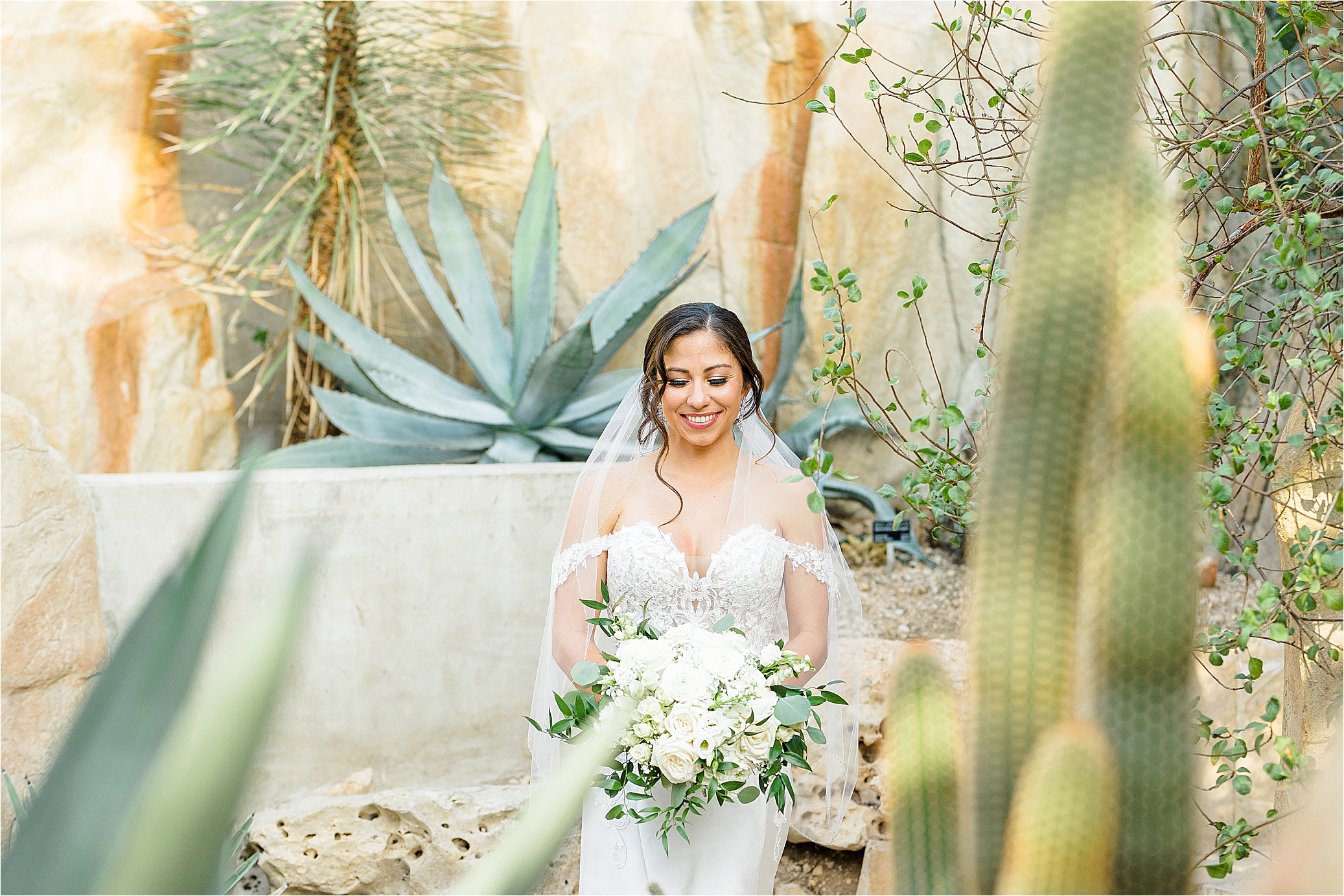 A bride smiles in front of desert greenery at San Antonio Botanic Garden during her bridal portraits with Jillian Hogan Photography 