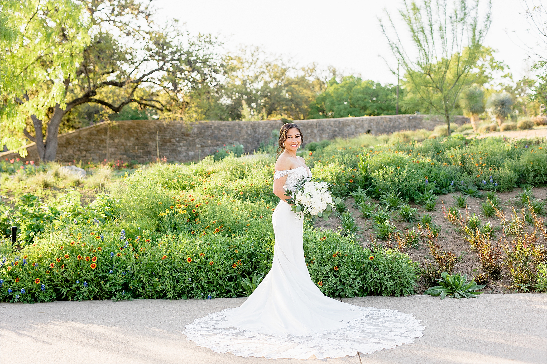 A bride smiles surrounded by flowers and greenery at San Antonio Botanic Garden during her Spring Bridal Portraits 