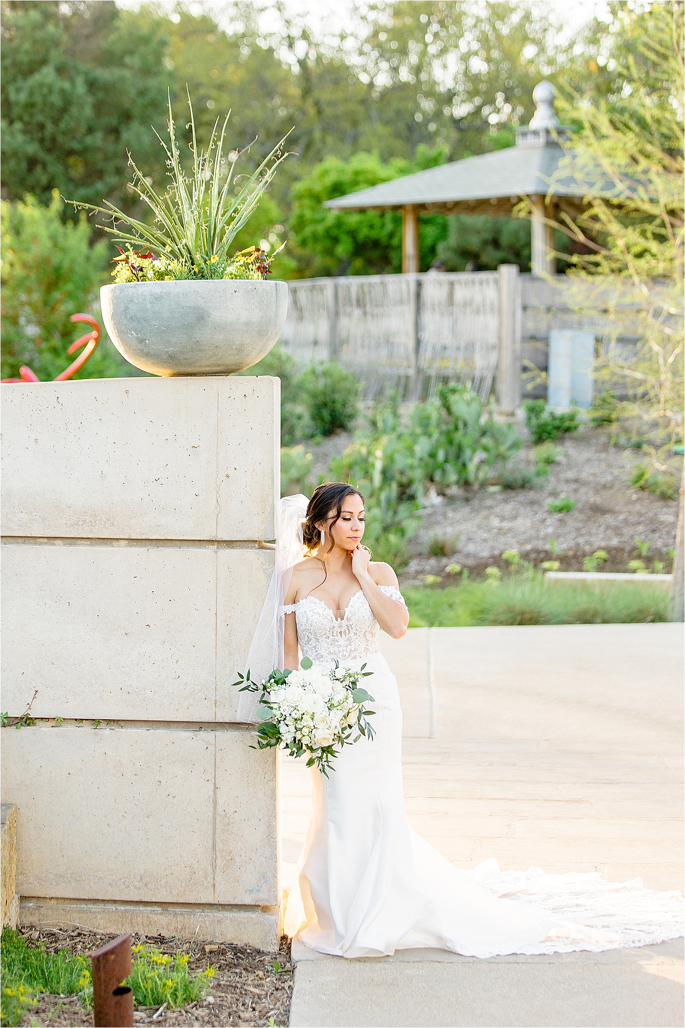 A bride poses leaning on a wall surrounded by greenery at San Antonio Botanic Garden during her bridal Session with Jillian Hogan Photography
