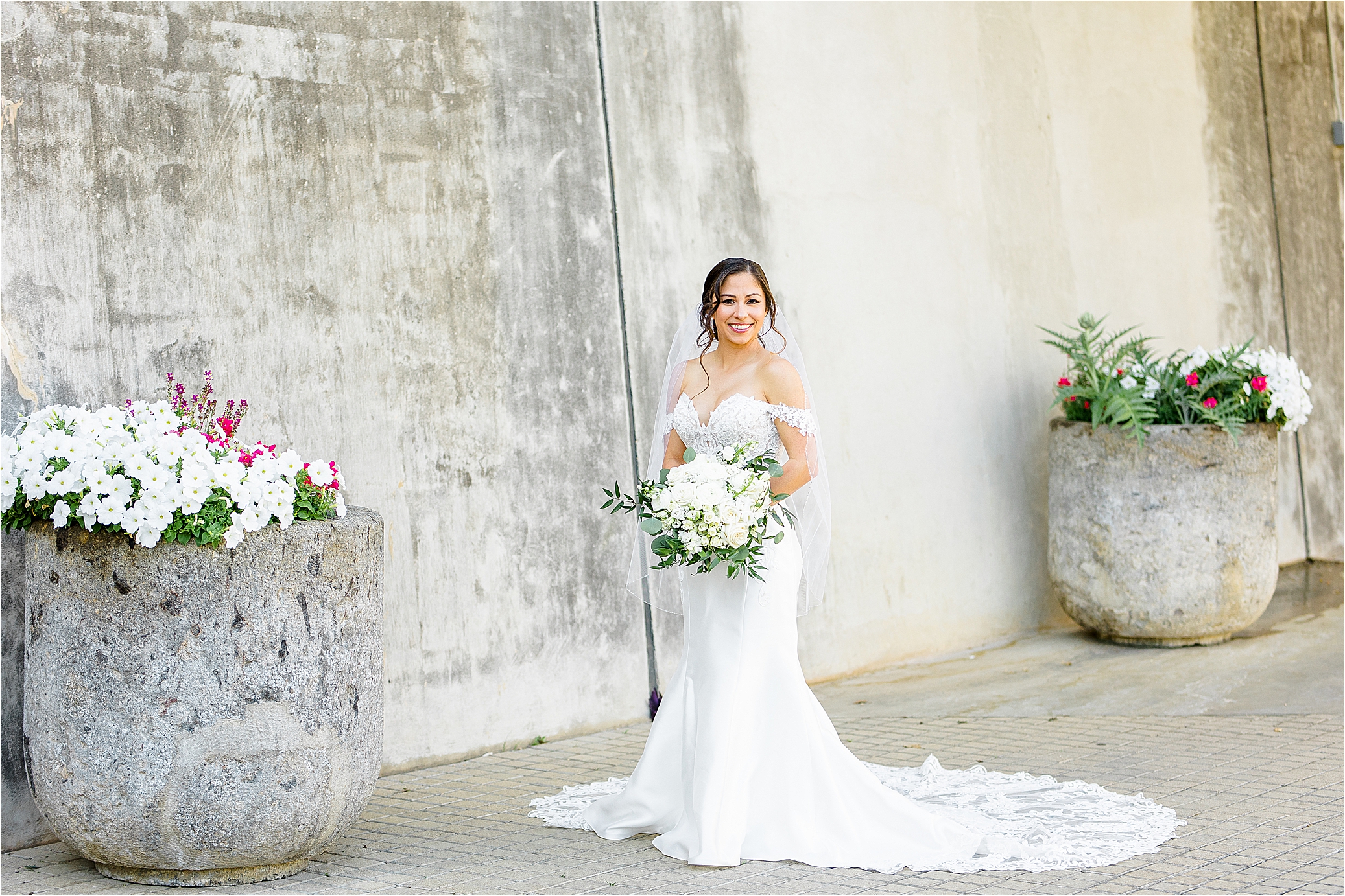 A bride smiles next to cement pillars of flowers during her spring bridal session at San Antonio Botanic Garden in San Antonio, Texas