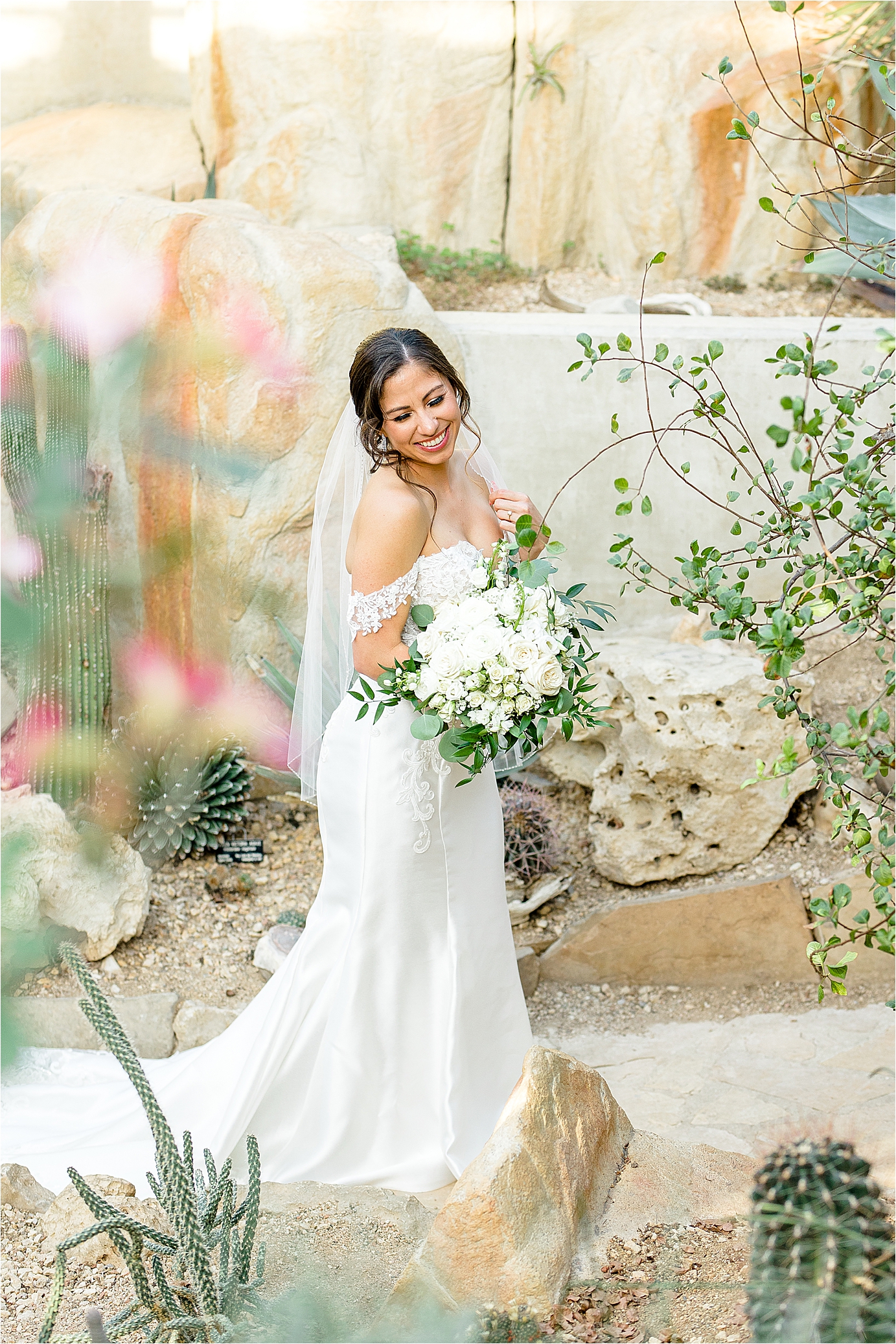 A bride smiles over her shoulder in front of desert vegetation at San Antonio Botanic Garden during her bridal portraits 
