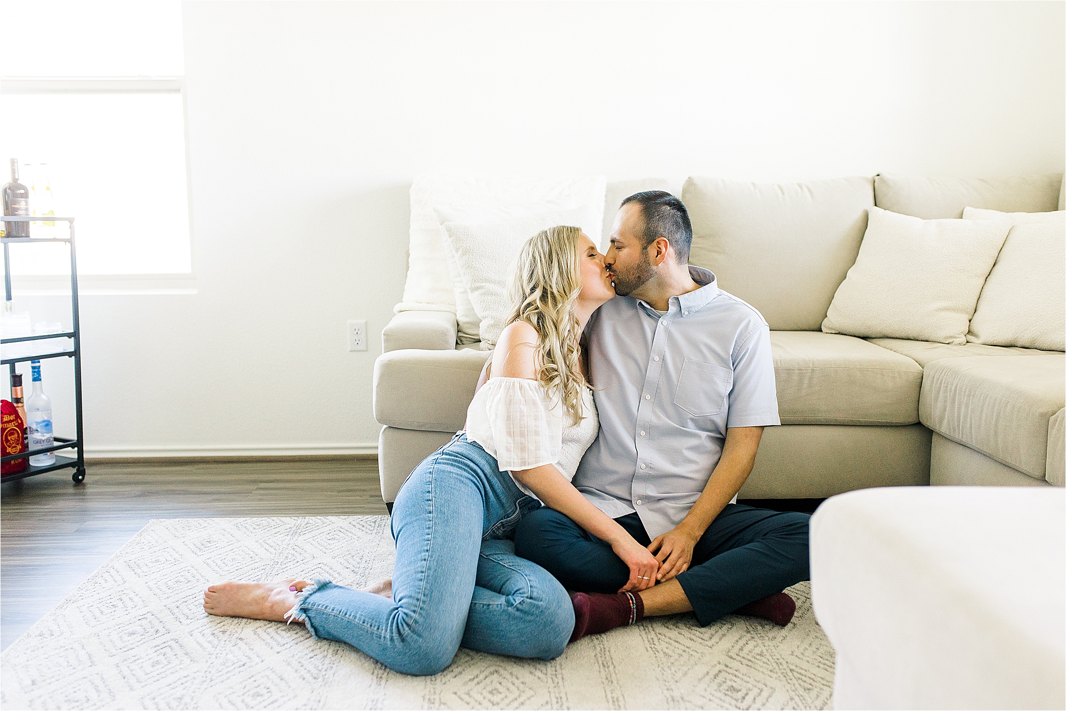 A couple shares a kiss sitting on the floor in their living room for their at home engagement session in South Austin, Texas