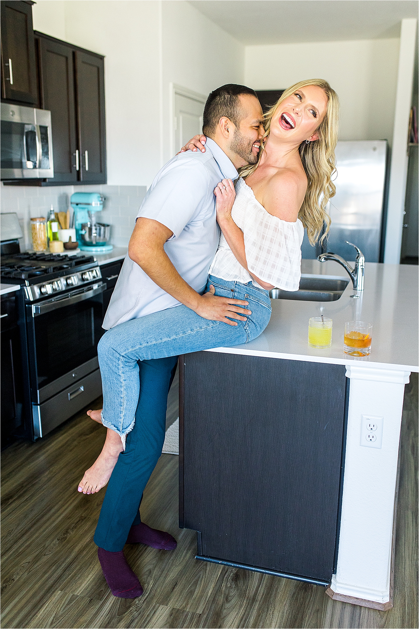 A couple sits on their kitchen and laughs during their at home engagement session in Austin, Texas