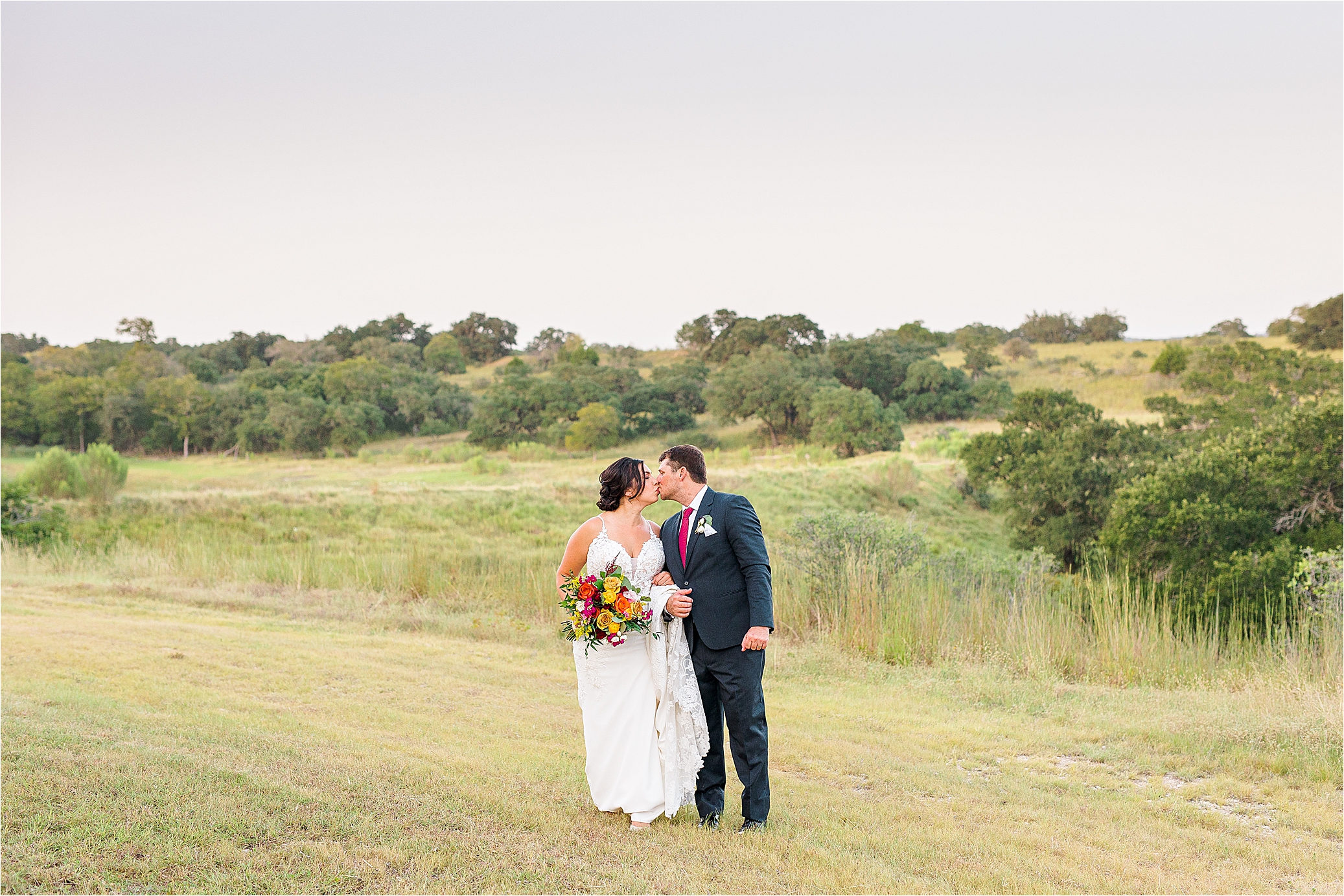 A couple kisses in front of Texas Hill Country on wedding day at paniolo ranch in Boerne, Texas