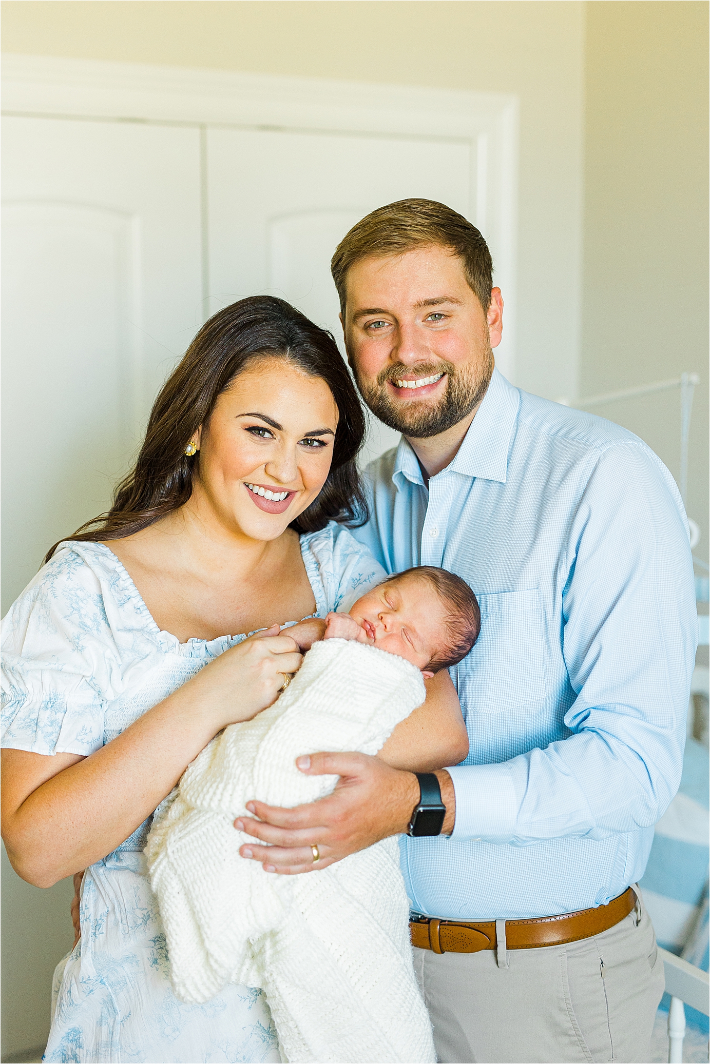 A couple cuddles their newborn baby close and smiles at the camera during their lifestyle newborn session with San Antonio Photographer Jillian Hogan