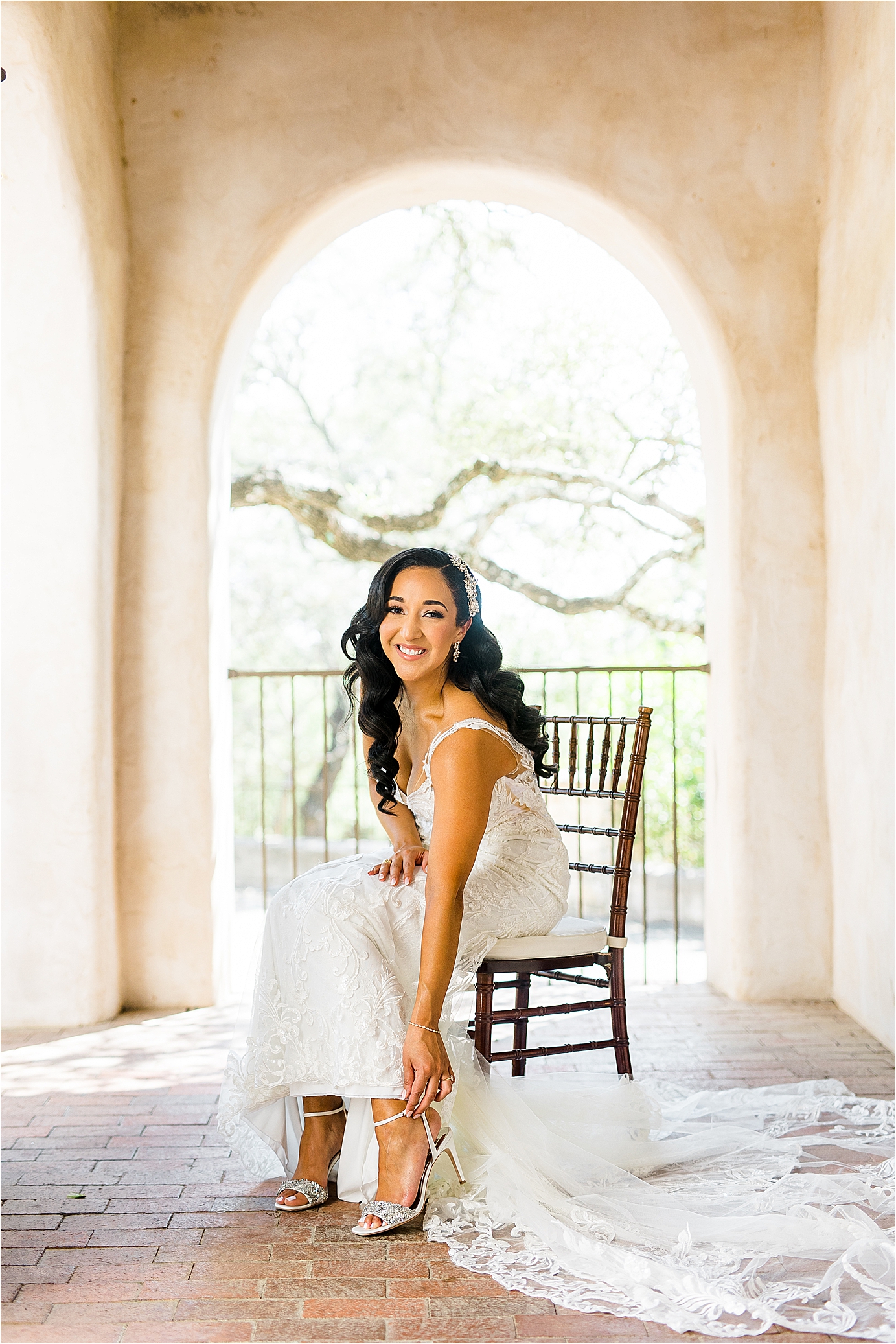 A bride sits and puts on her shoes in front of a pretty arch at Lost Mission on her wedding day in Texas Hill Country 