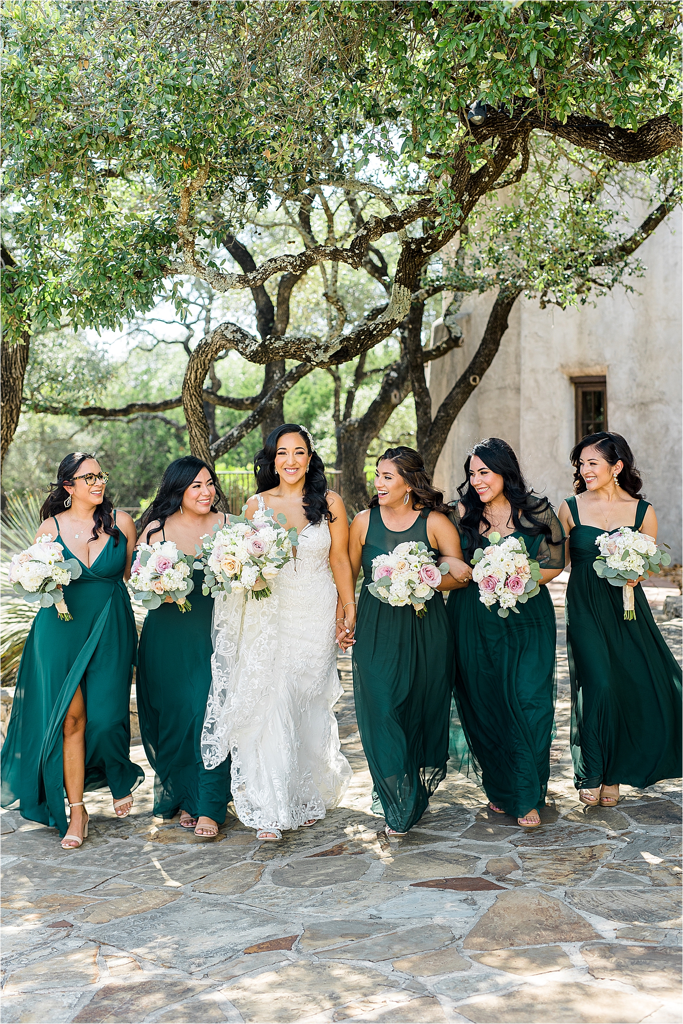 A bride walks hand in hand with her bridesmaids in front of Lost Mission Chapel in Texas Hill Country 